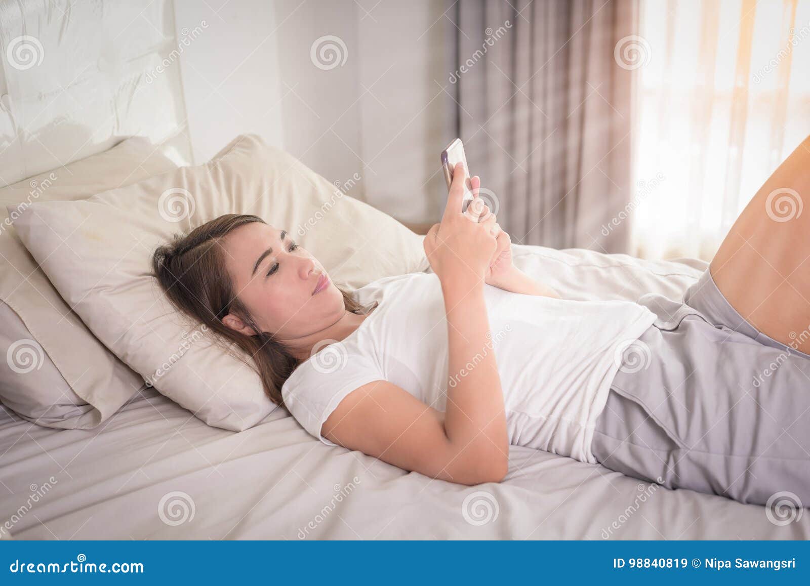 Smiling Woman Looking At Mobile Phone Lying Down On White Bed H Stock Image Image Of Apps 