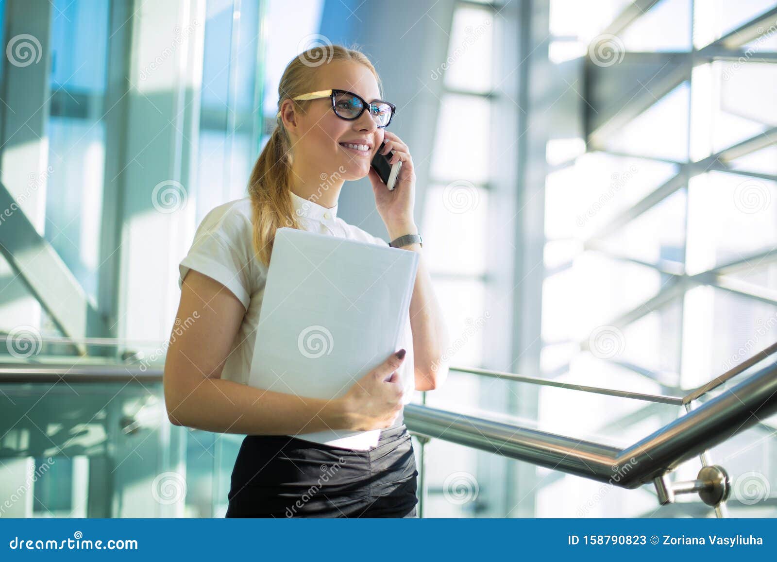 smiling woman professional jurist in formal wear and paper documents in hand having pleasant mobile phone conversation