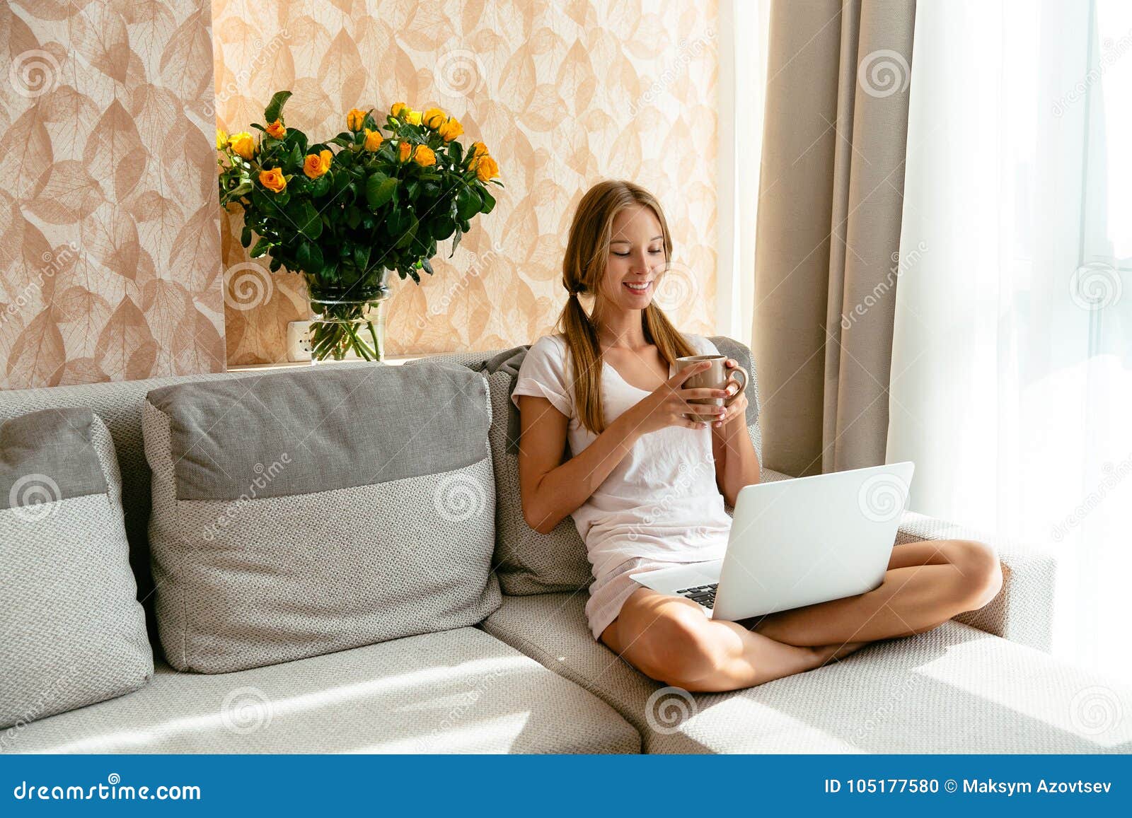 woman with cup of tea watching movie on laptop at home