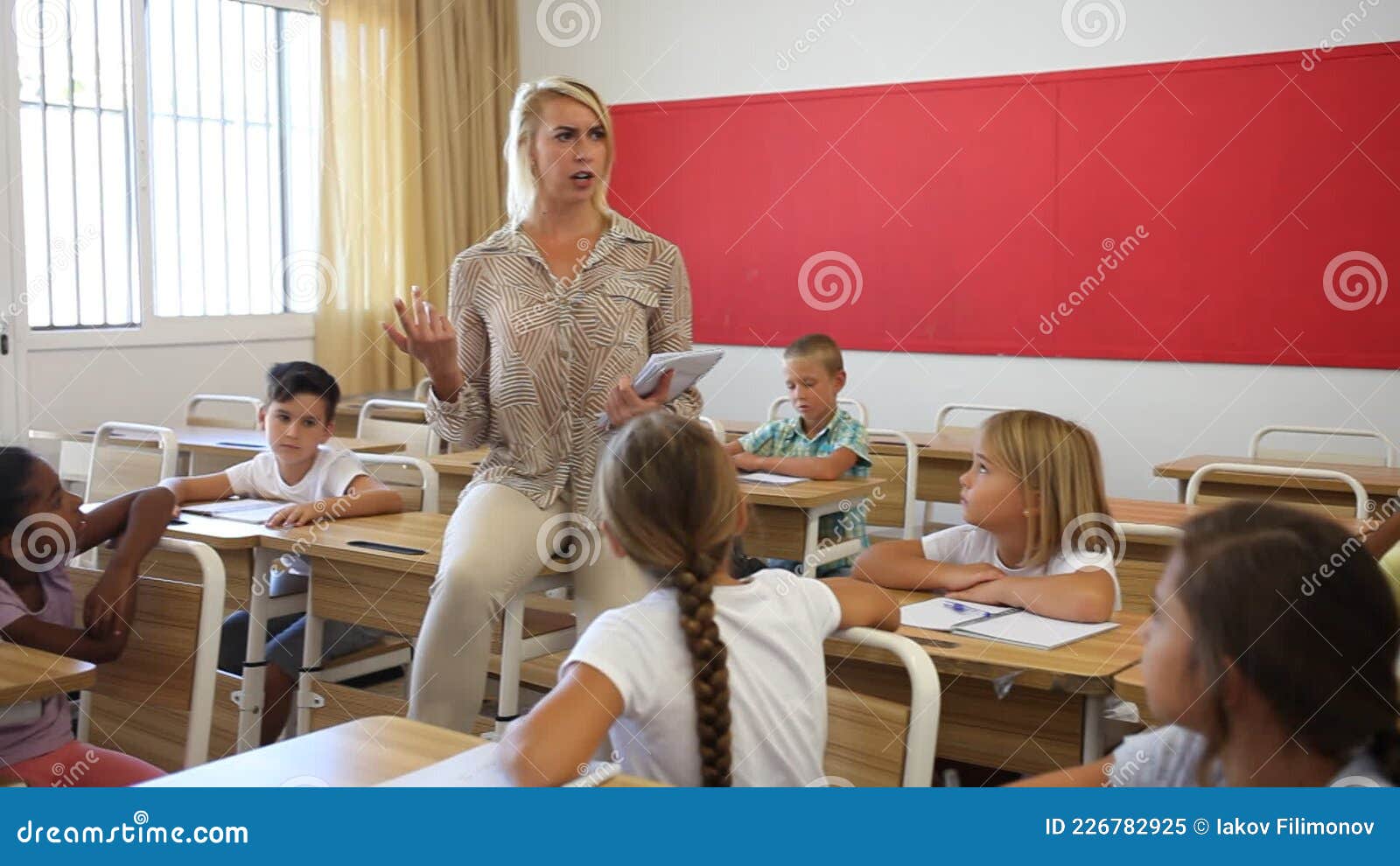 Female Teacher Talking With Primary School Pupils In Classroom Stock