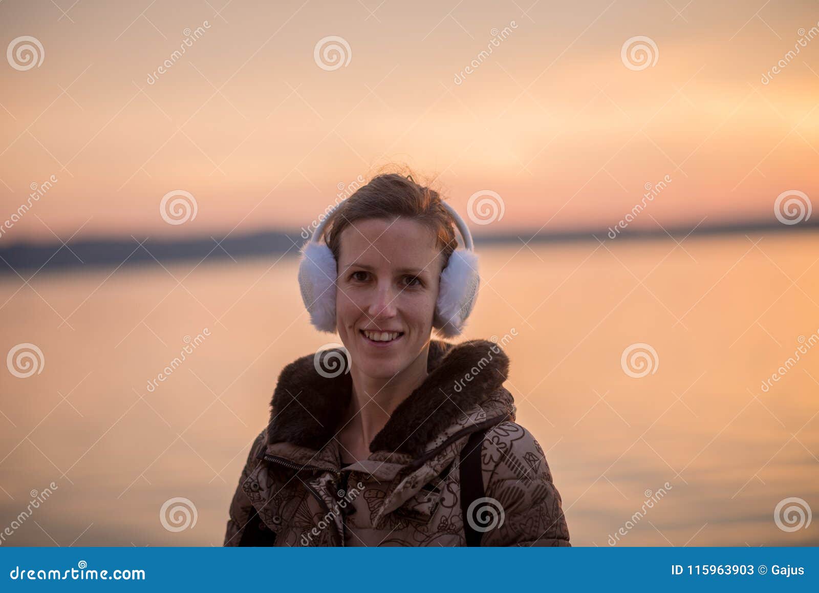 smiling woman wearing fluffy ear muffs at sunset