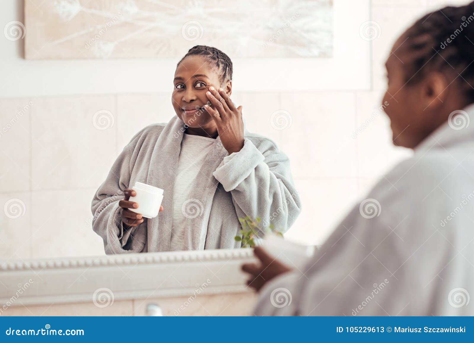 young african woman applying face cream in the bathroom
