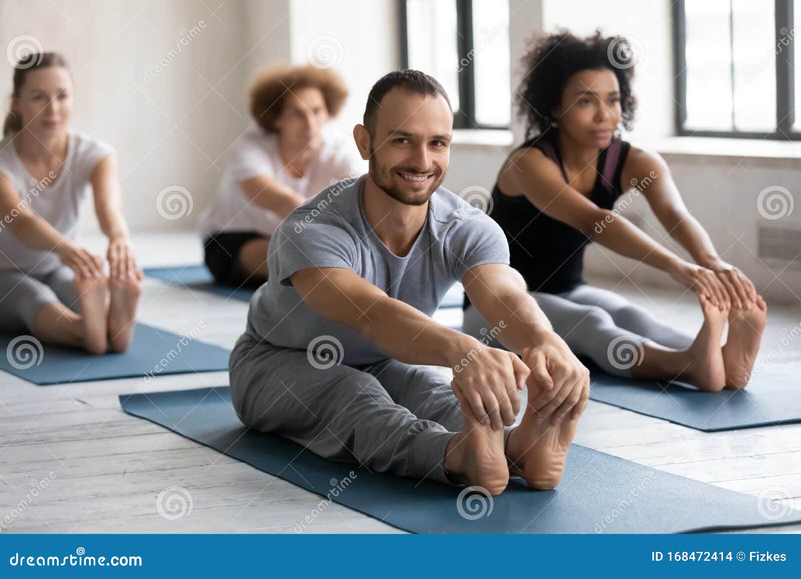 smiling man practicing yoga at group lesson, seated forward bend