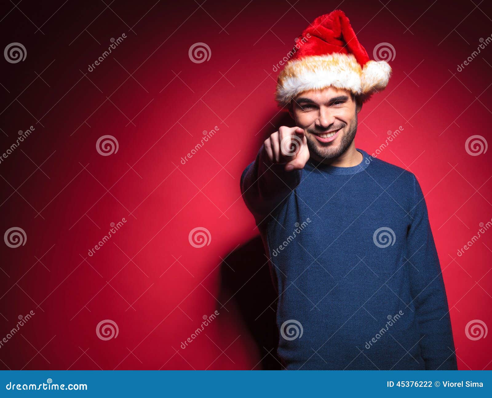 Smiling young santa pointing at you against red background.