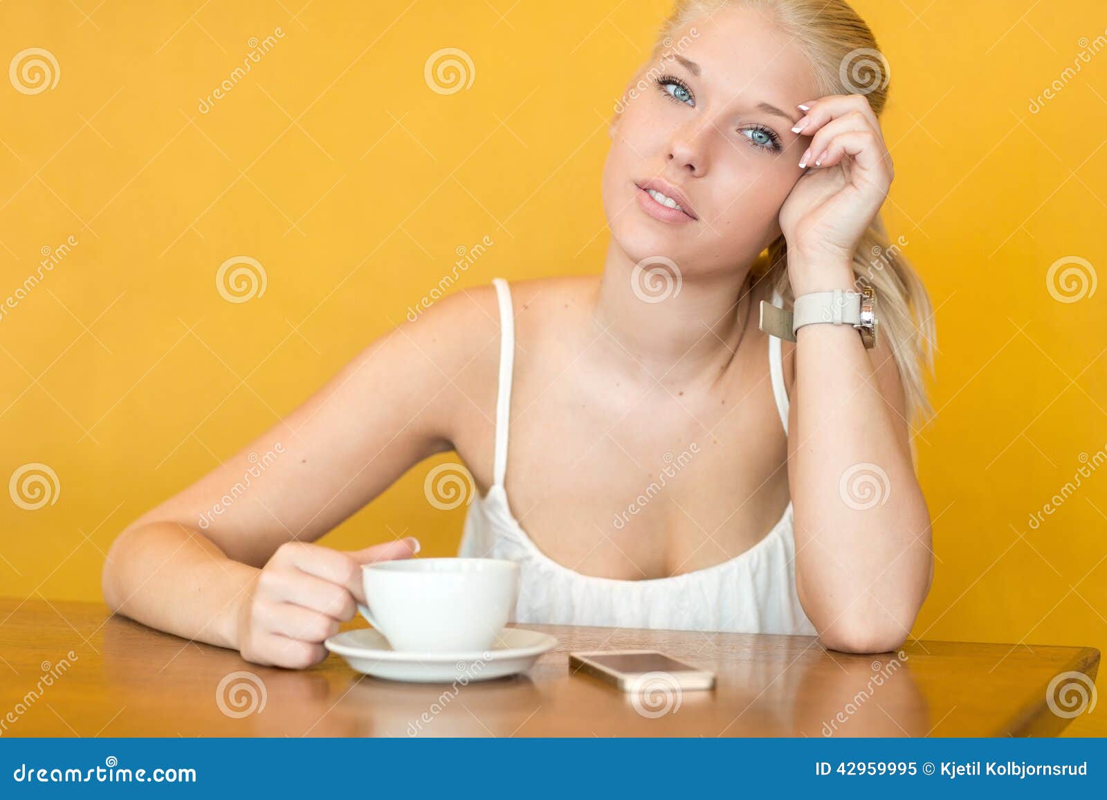 Smiling young woman drink coffee at cafe. Smiling beautiful blonde teen girl using phone and drinking coffee or tea at a cafe.