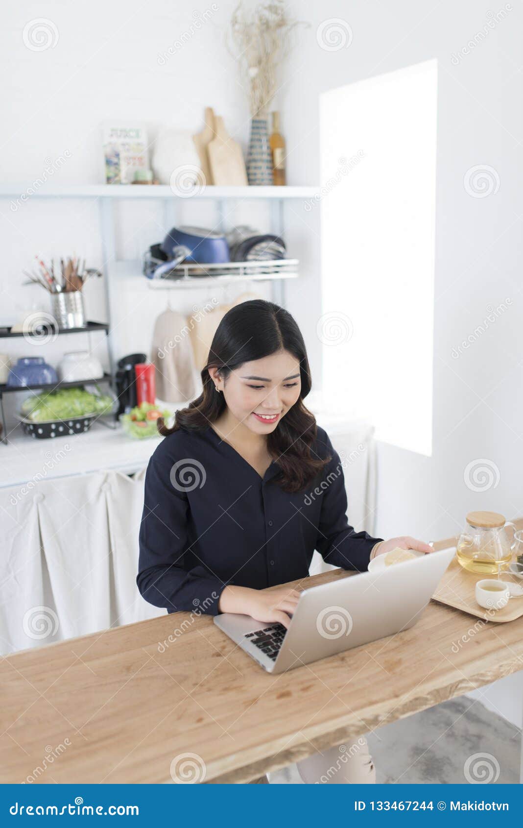 smiling young woman using laptop in the kitchen at home