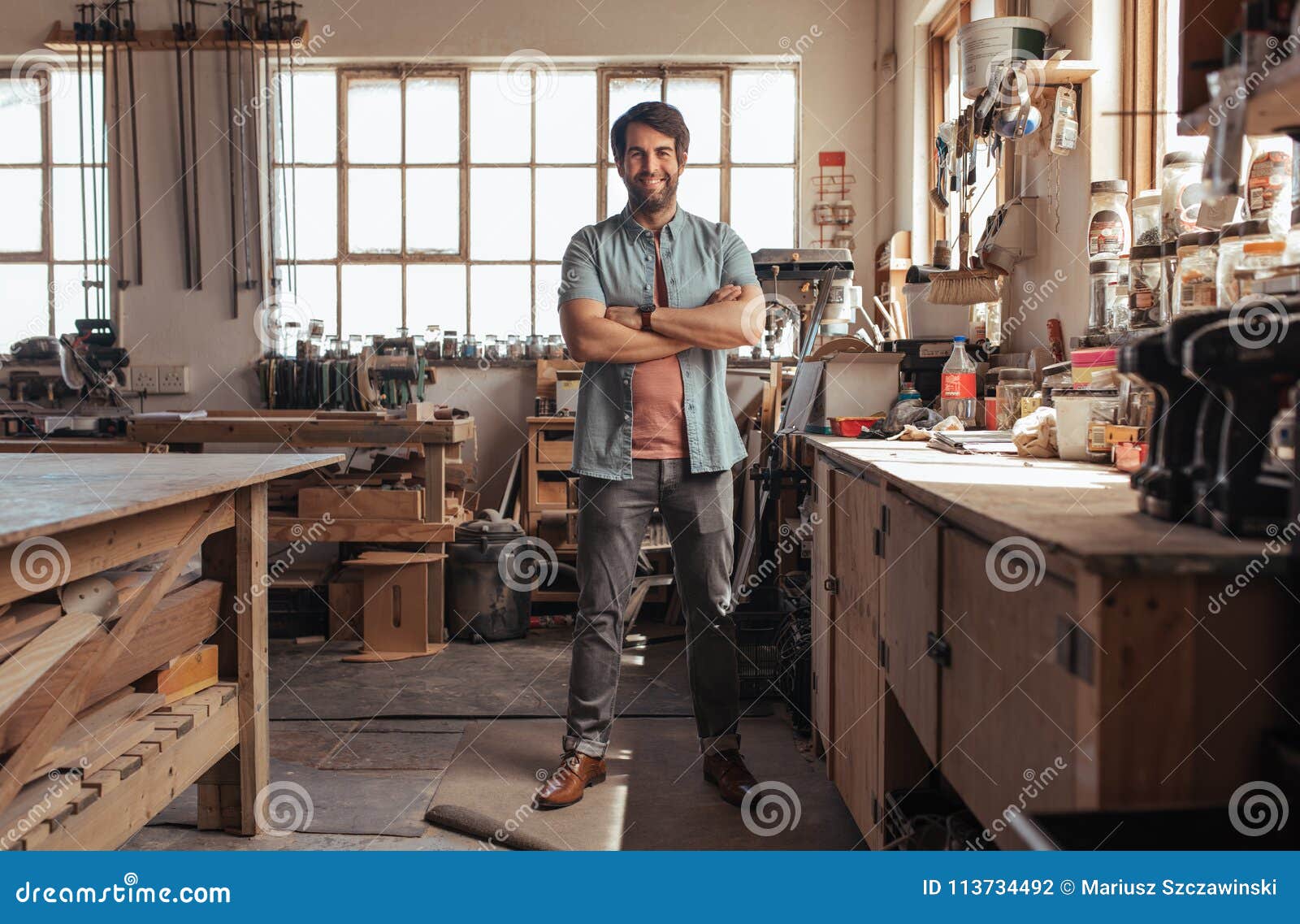 smiling young woodworker standing in his workshop full of tools