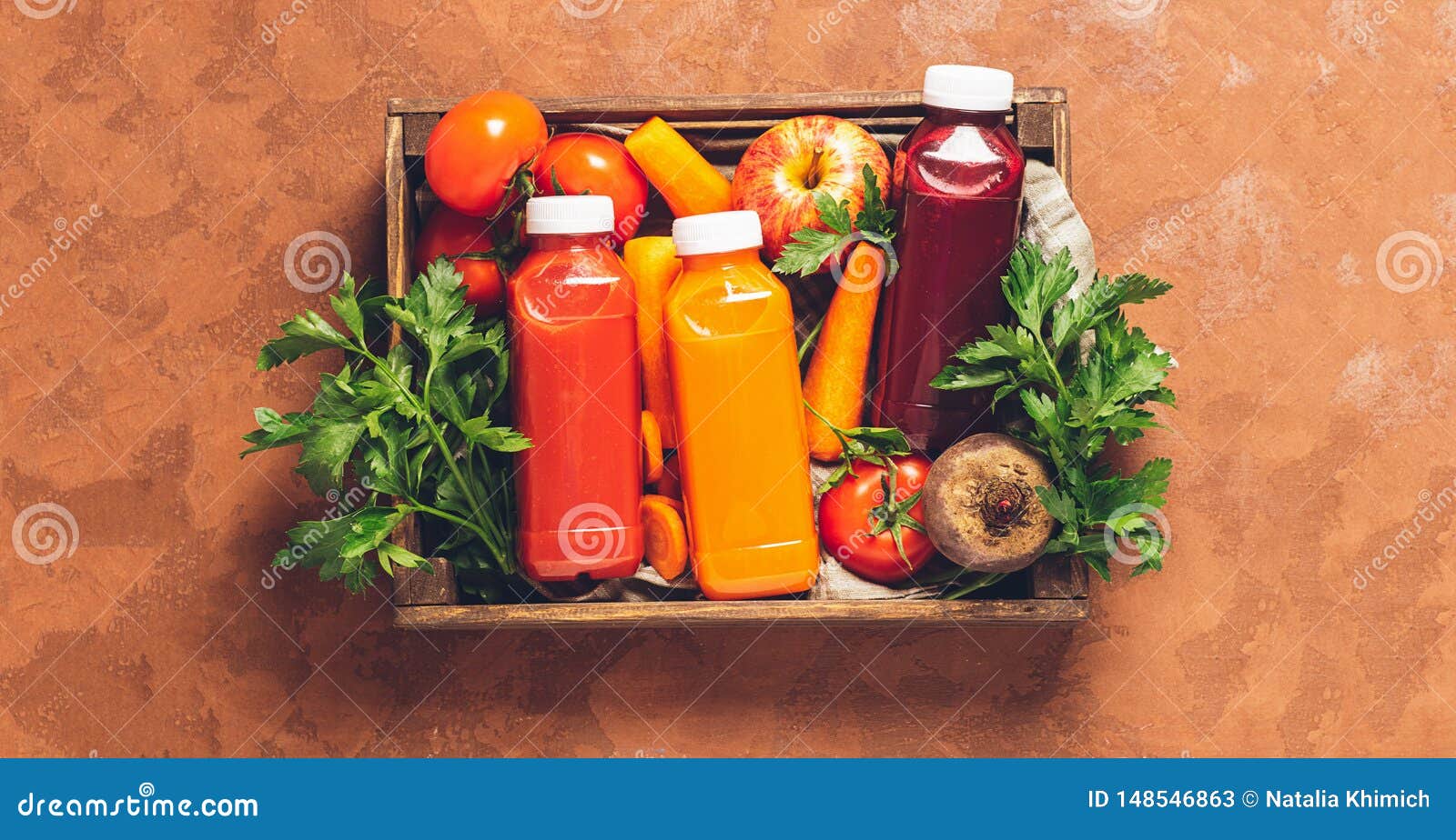 Fresh juice smoothies from a variety of vegetables carrots apple tomatoes beets bottles in wooden box brown background. Fresh juice smoothies from a variety of vegetables carrots apple tomatoes beets in bottles in a wooden box on a brown background. Top view flat layout. Copy space. Horizontal frame