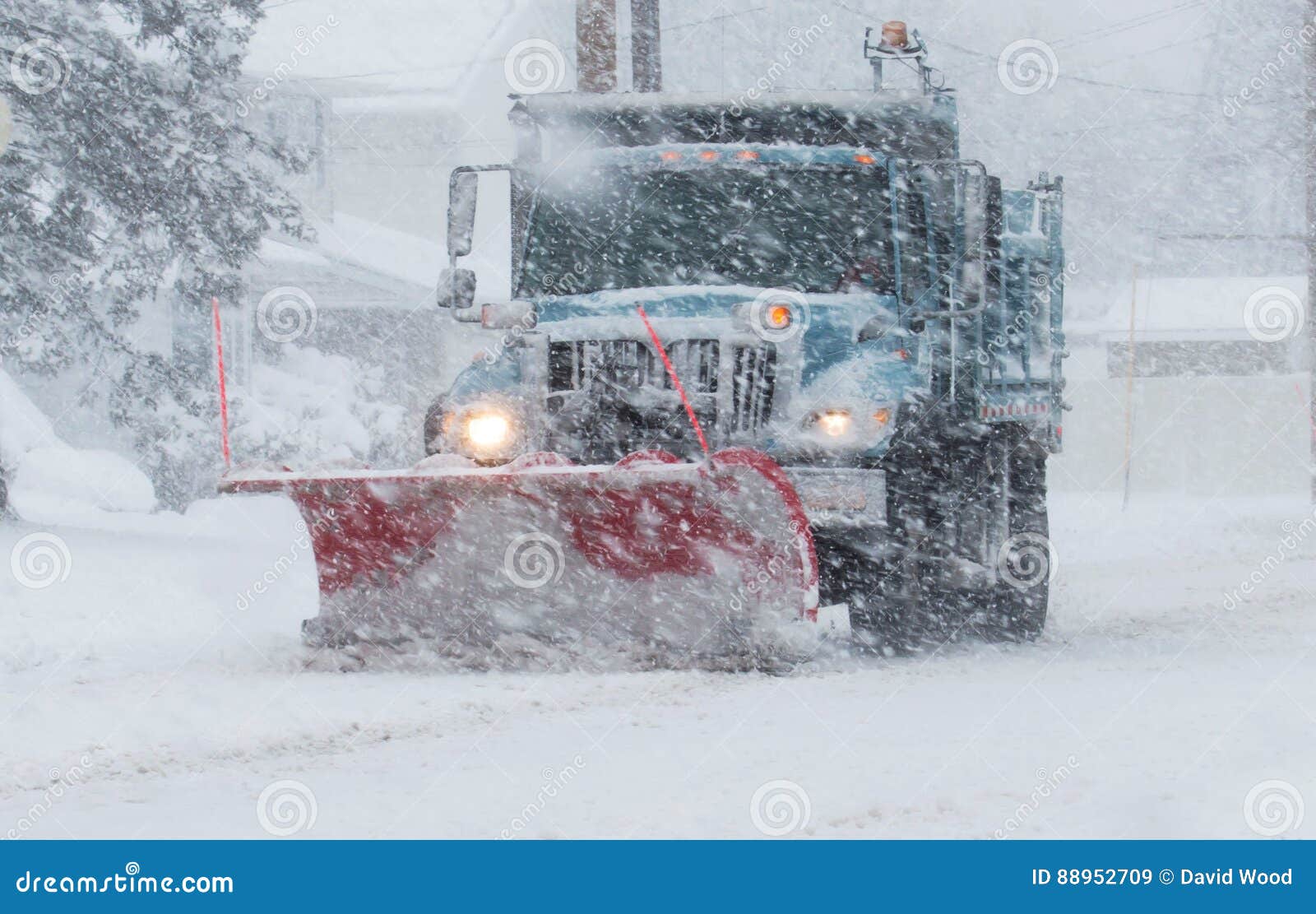snow plow with a red plow working in a blizzard
