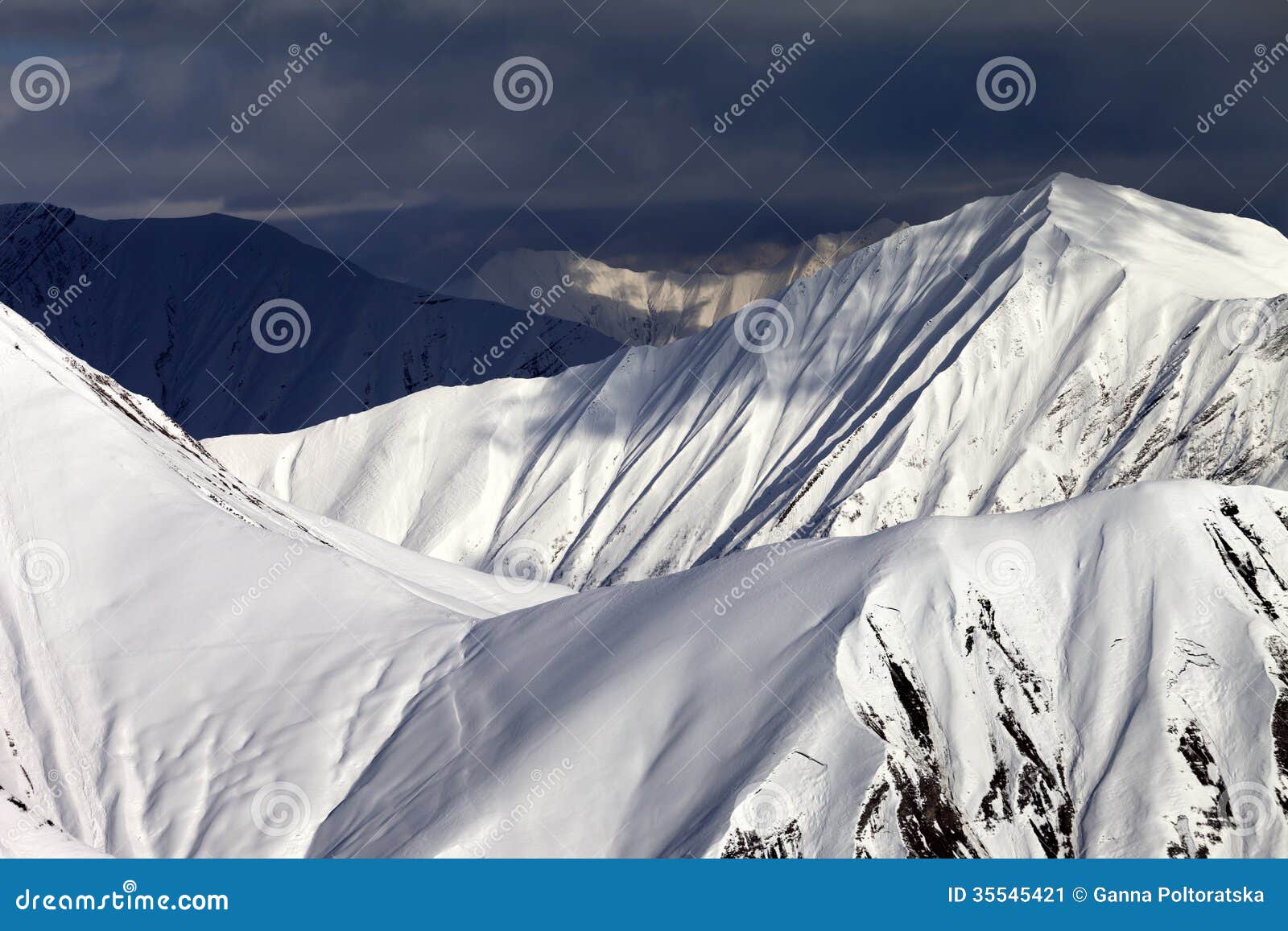 Snowy sunlit mountains and overcast sky. Caucasus Mountains, Georgia, view from ski resort Gudauri.