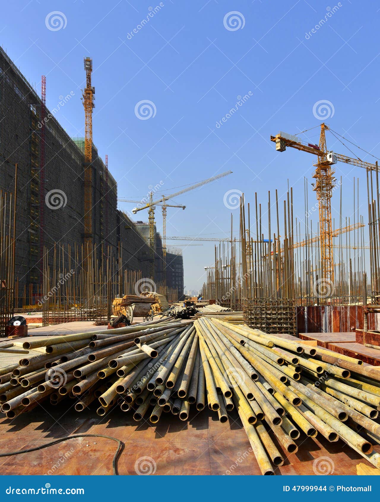 Sob o canteiro de obras, na construção de grandes construções. Tubos de aço amarelos das tubulações de aço na construção do grande canteiro de obras moderno de Œunder do ¼ do buildingsï guindaste de torre, rooter, motorista de pilha, máquina, reforço da malha, andaime de construção, para colocar as fundações