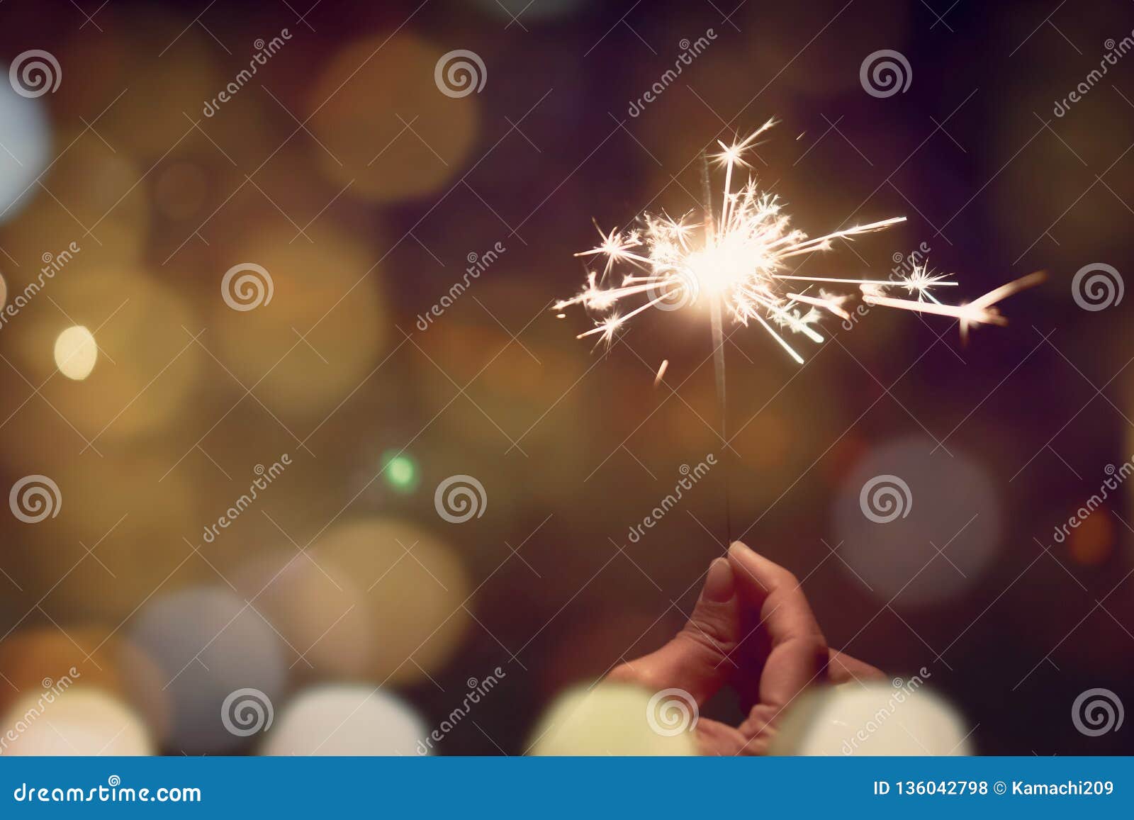 Soft focus of woman hand holding bright christmas sparkle on nature night beach. Bokeh light is the background