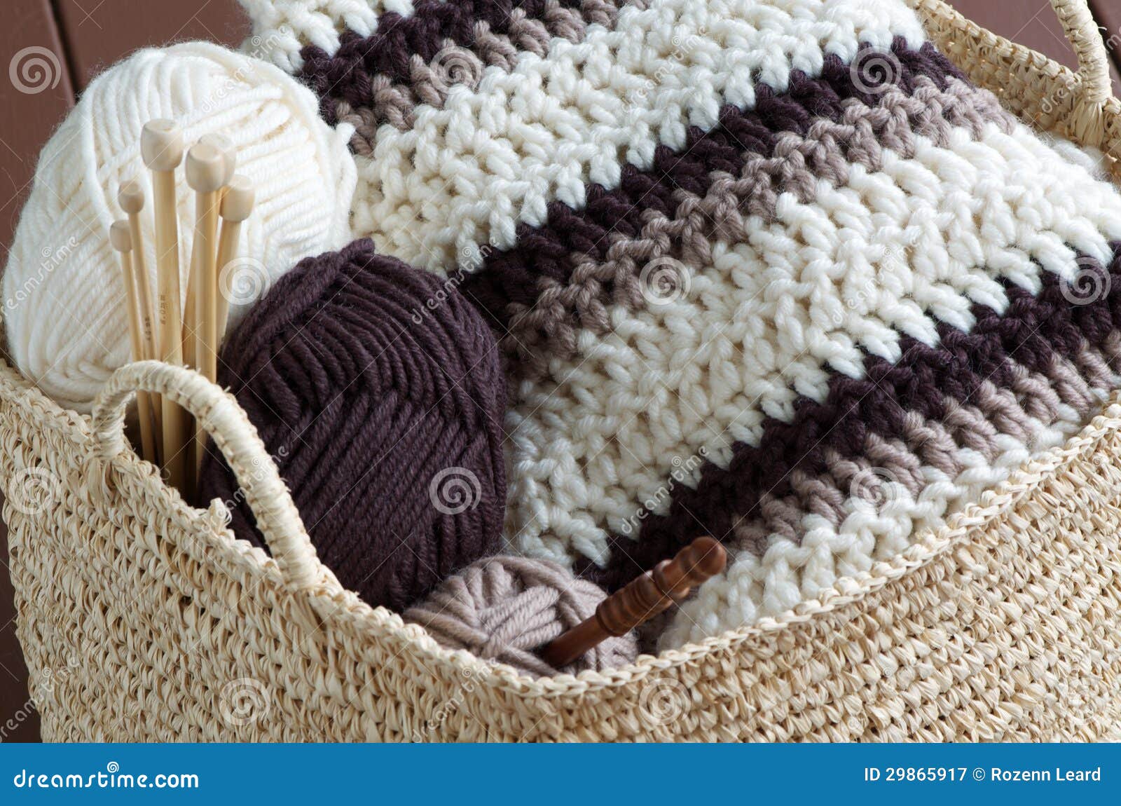 Knitting. Wicker basket with colored balls of wool yarn and crochet hooks  on wooden background. Stock Photo