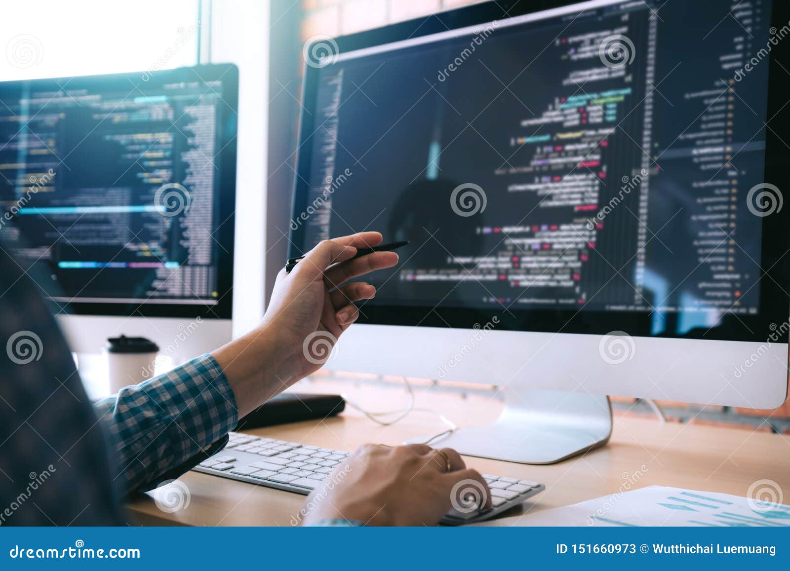 software developer holds the pen pointing to the computer screen and is analyzing the code