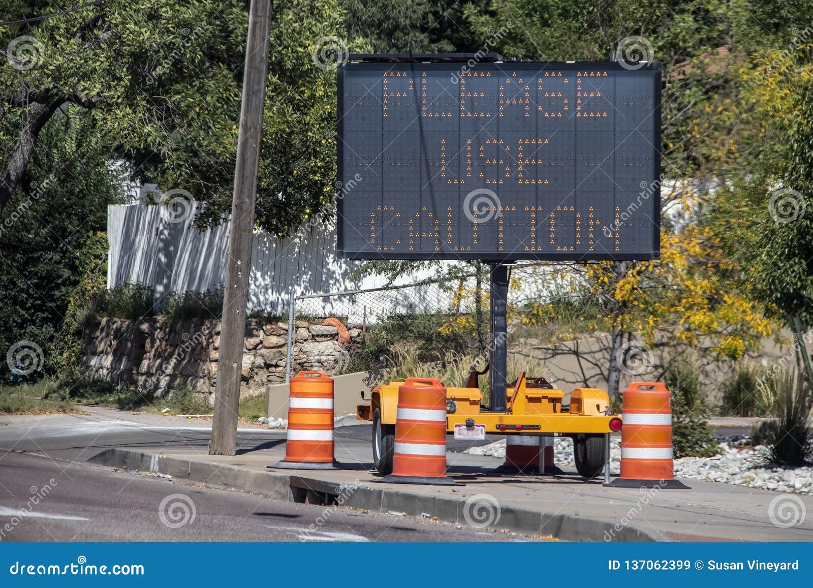 solar mobile sign with orange cones sitting on sidewalk besides road saying please use caution - selective focus