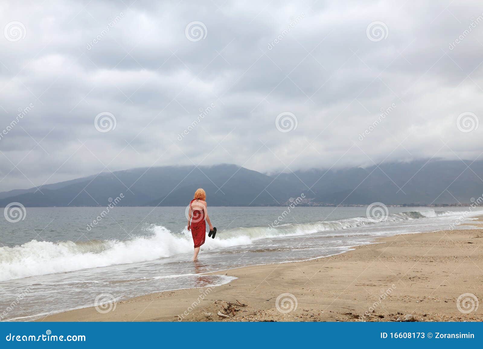 Soledad. Mujeres caucásicas vestidas rojas que recorren en una playa