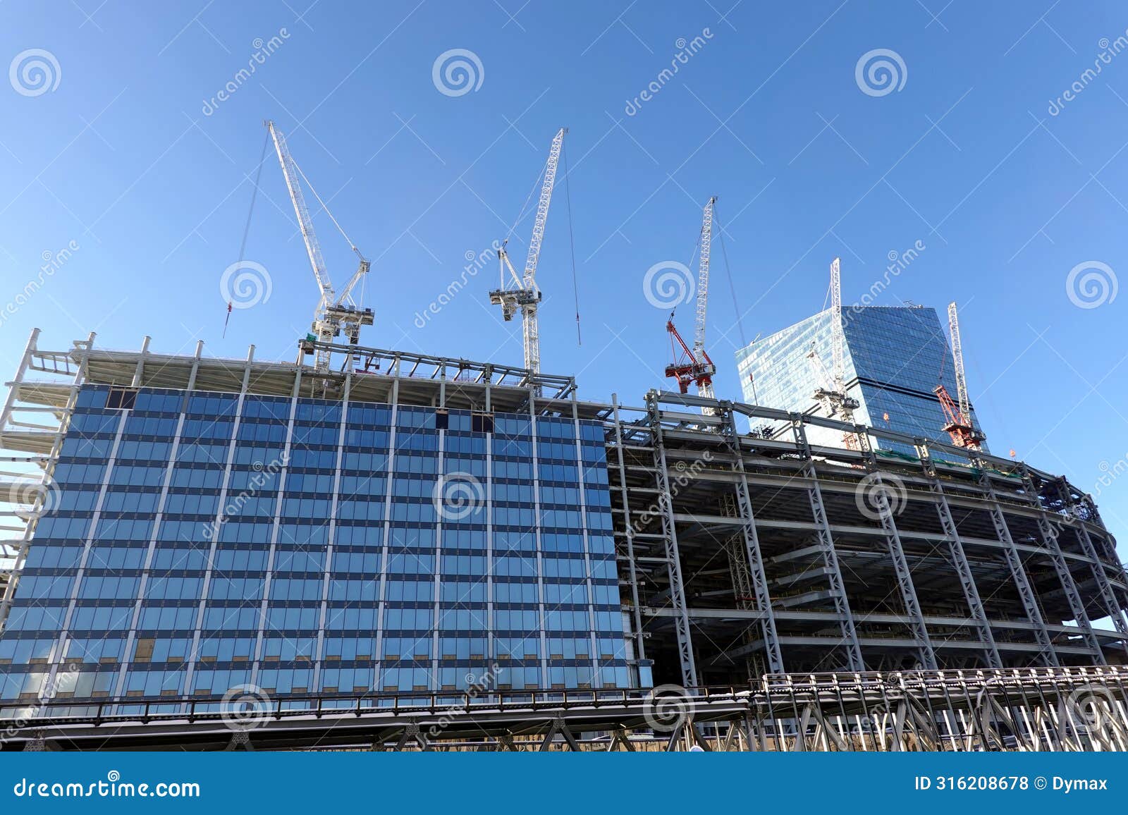 some tower cranes are building a modern tall skyscraper against clear cloudless blue sky