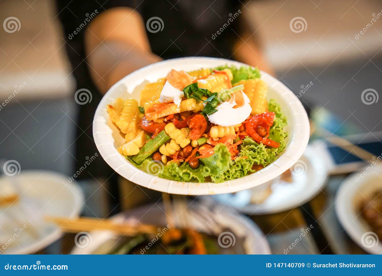 somtum; spicy papaya salad with boiled corn in paper dish at foodtruck street food event., bangkok, thailand