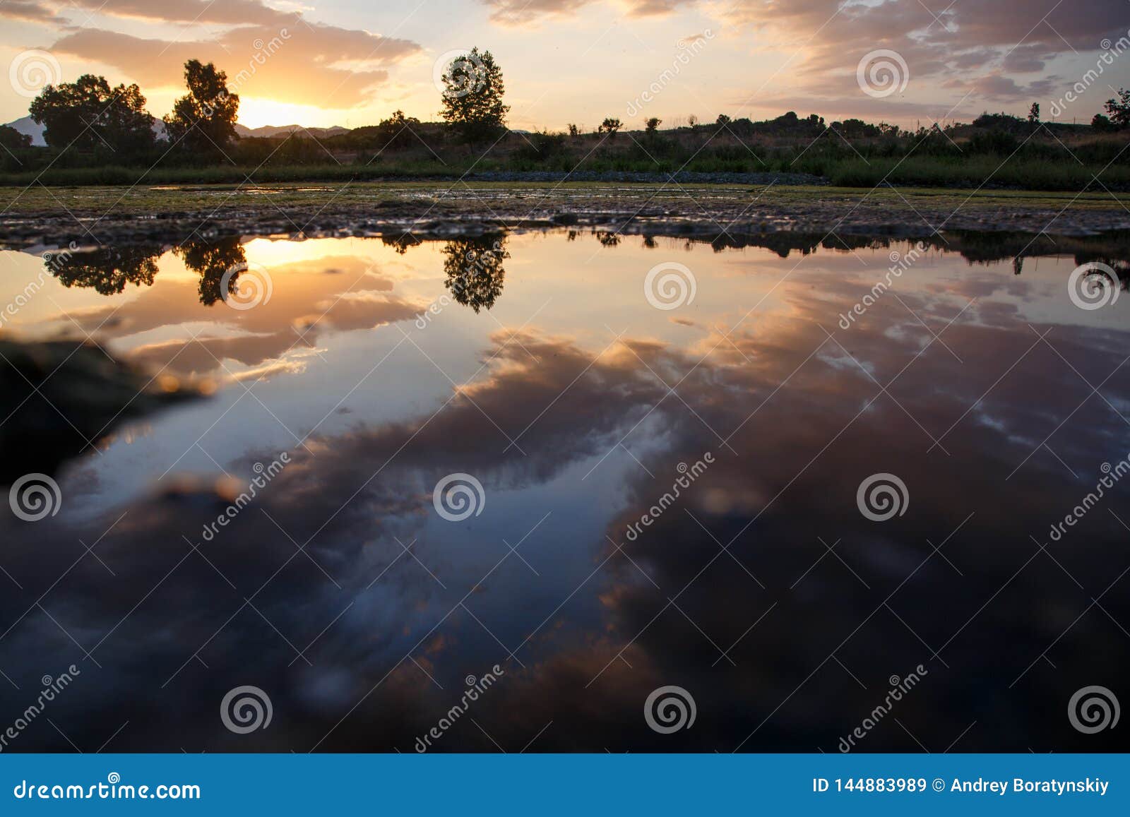 Sonnenuntergang mit den Wolken und Bäumen nachgedacht über das Wasser von einem See