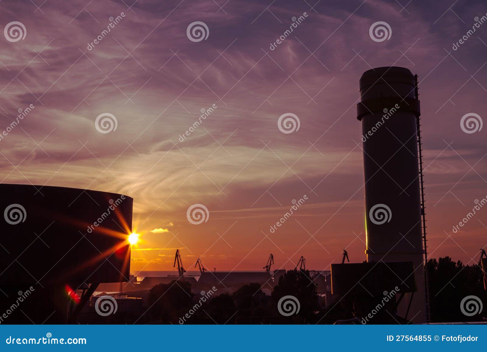 Sonnenuntergang über der Triebwerkanlage. Ansicht über drastischen Sonnenuntergang über dem Stadtkanal mit Kränen im bakcground mit Schattenbild des Kamins und prüfende Antriebswelle des Co-Erzeugung flechten im Vordergrund