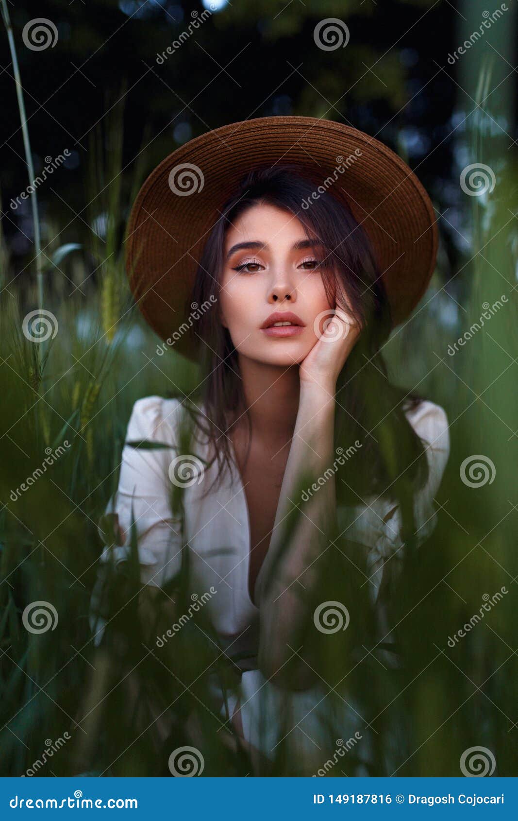 Sorglose entz?ckende brunette junge Frau in der romantischen Ausstattung, mit der Hand auf ihrem Gesicht auf dem gr?nen Gebiet Fr. Beautiful Young Woman seated in the field in green grass, looking at camera with attitudine. Outdoors. Enjoy Nature. Healthy look girl on spring lawn. Allergy free concept. Freedom.