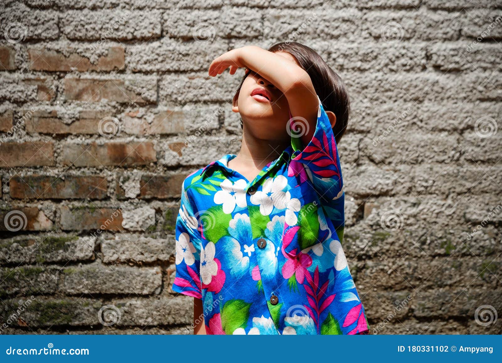 southeast asian ethnicity little boy sunbathing in the morning at the backyard at home. hand raising up to cover her face