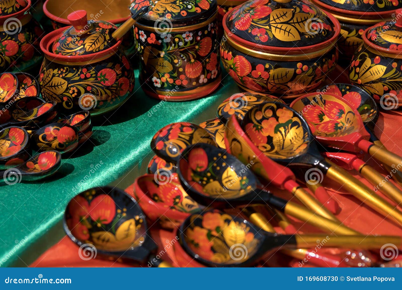 souvenir painted wooden spoons and caskets with floral patterns lie on red with green shiny material