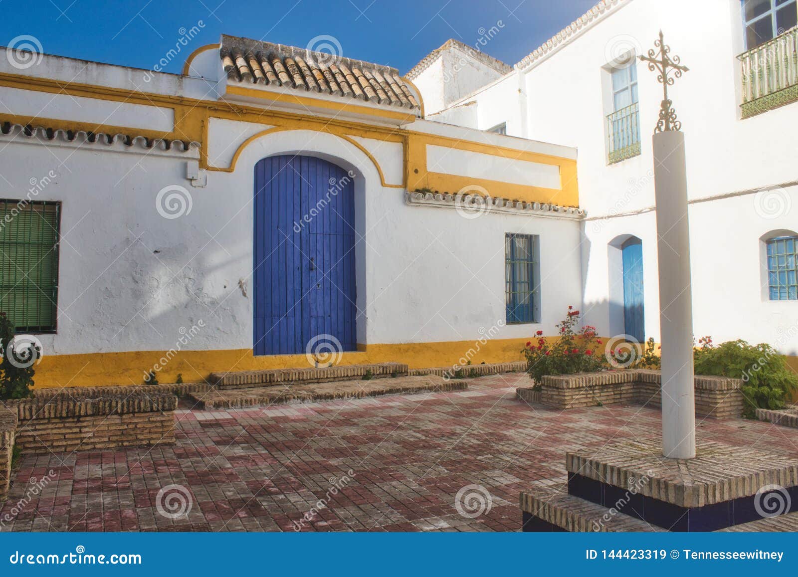 spanish brightly colored courtyard in the sun with an ornate cross on a column
