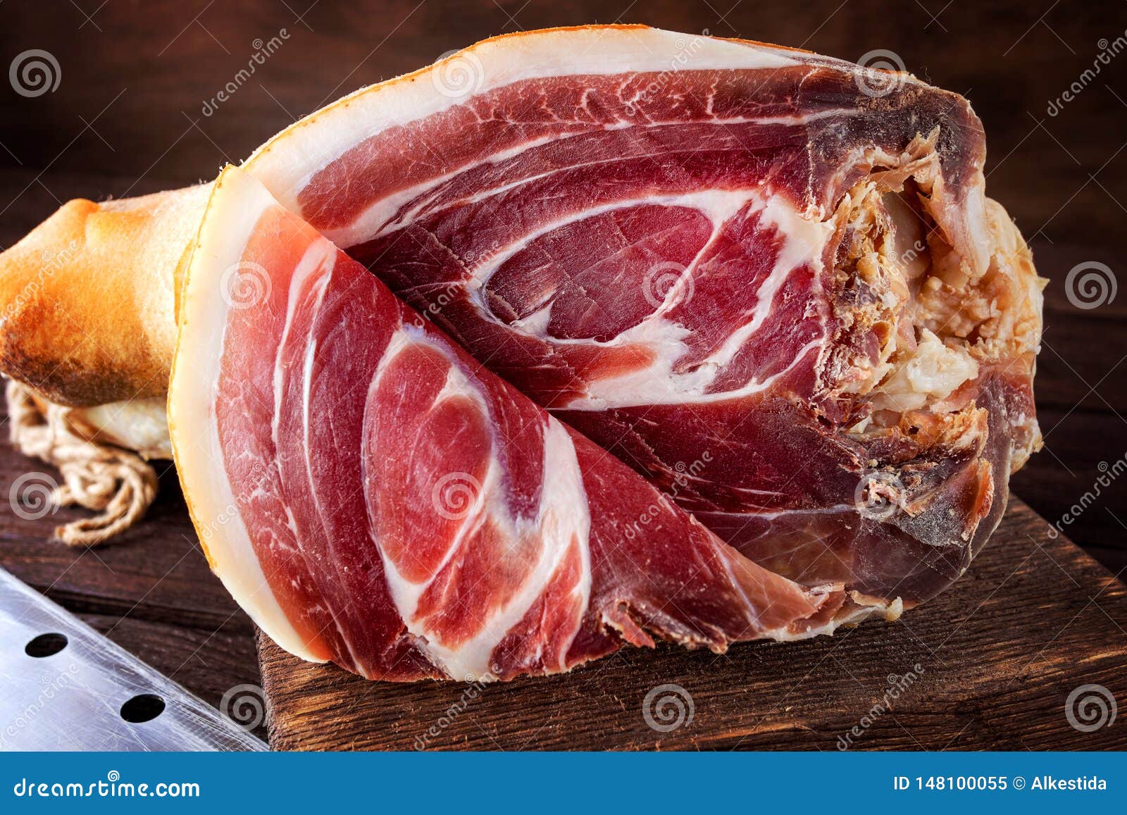 spanish ham, bellota, jamon serrano, crudo, italian prosciutto, whole leg,  parma ham cut with a knife and lying on a wooden board