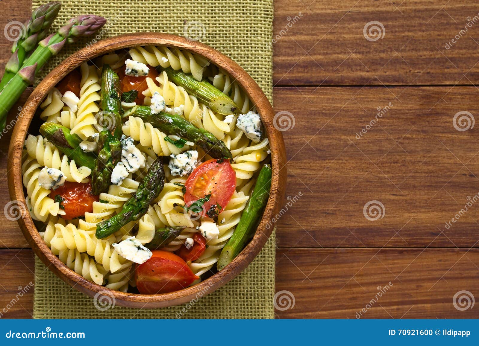 Sparris-, tomat-, ädelost- och pastasallad. Sallad för bakad grön sparris, för den körsbärsröda tomaten, ädelost- och rotinipastatjänade som i träbunken, fotograferad fast utgift på mörkt trä med naturligt ljus (selektiv fokus, fokusen på överkanten av salladen)