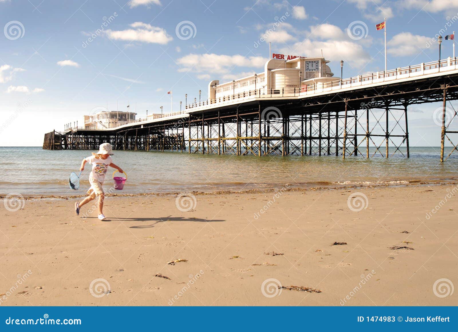 Spaß an der Küste. Kleines Mädchen, das den Sand im Schatten eines Sussex-Piers genießt