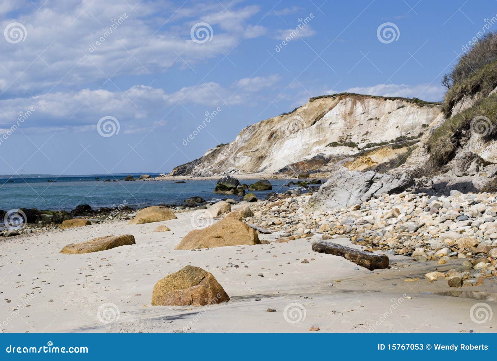 Spiaggia della Nuova Inghilterra. Una vista scenica di Aquinnah, o spiaggia di Gayhead in Martha's Vineyard. Le scogliere del mare dell'argilla con la spazzola verde sparsa incontrano la sabbia roccia-sparsa ed il mare blu con un cielo blu parzialmente nuvoloso in inizio dell'estate. Una destinazione popolare dell'isola per le vacanze della Nuova Inghilterra.