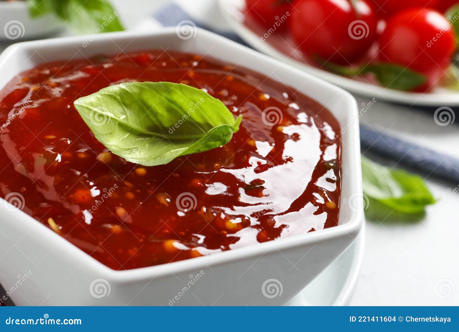 Spicy Chili Sauce with Basil on Light Table, Closeup Stock Photo