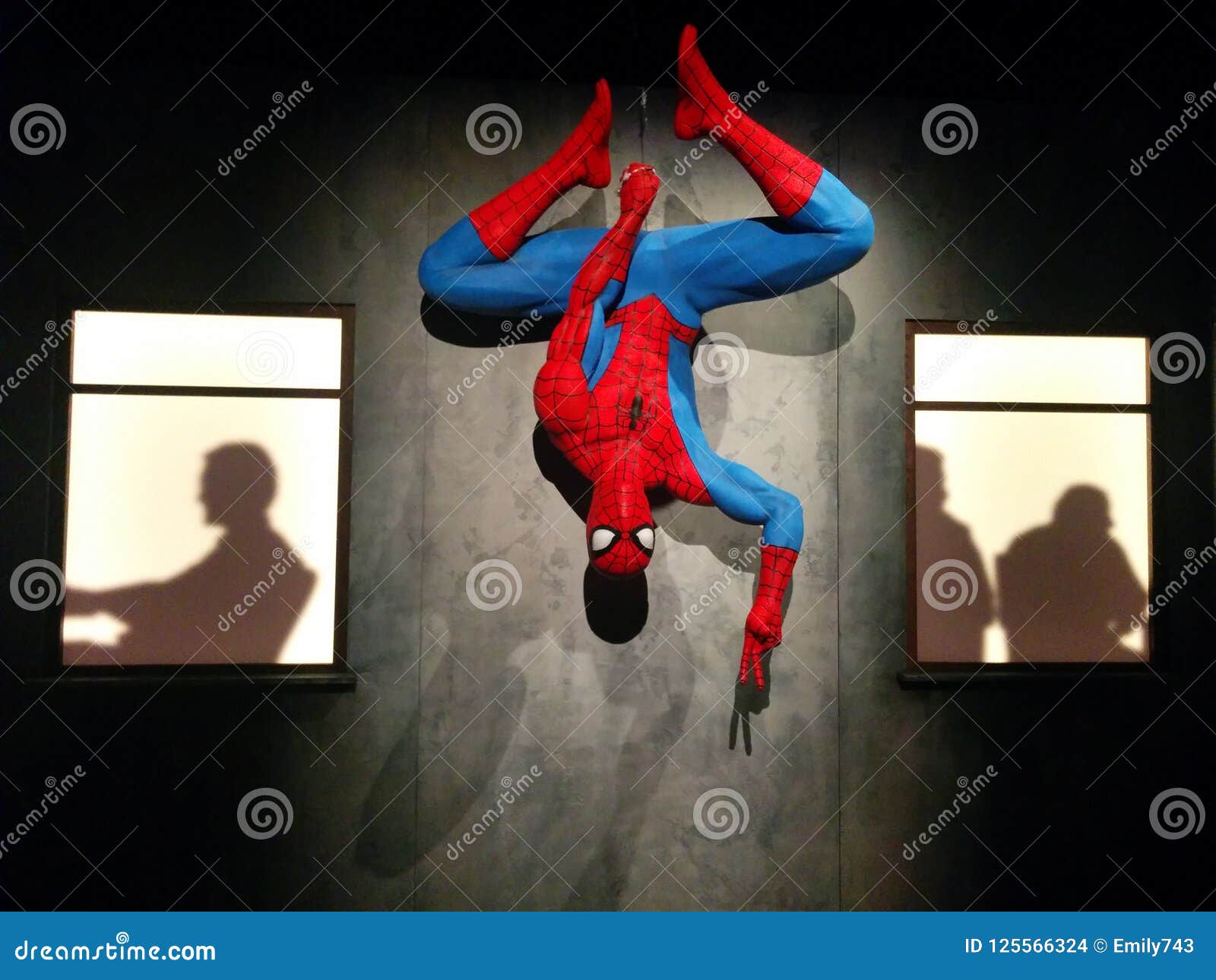 Spider-Man hanging upside down and giving the peace sign between two window...