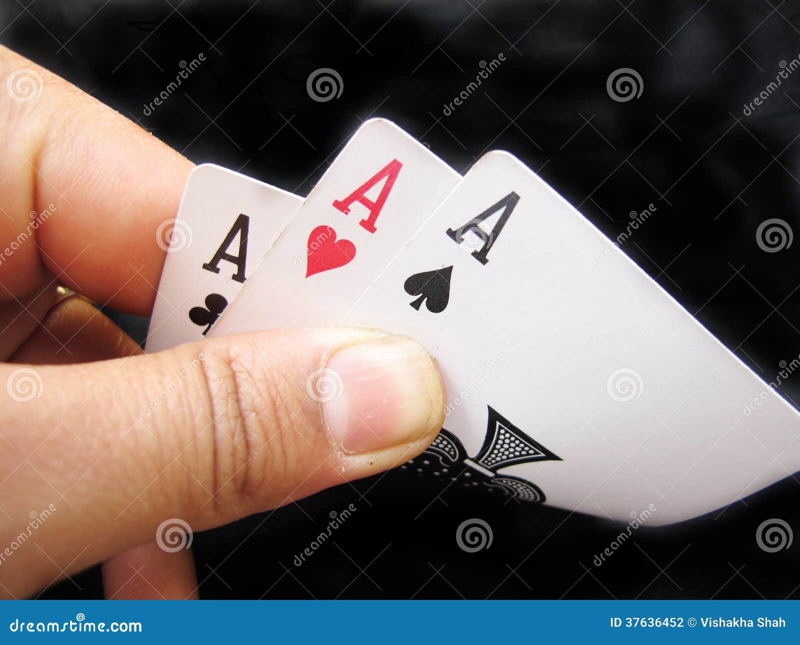 Spielen von Karten--Dreiassen. Hände, die drei Asse von Spielkarten auf Schwarzem halten.