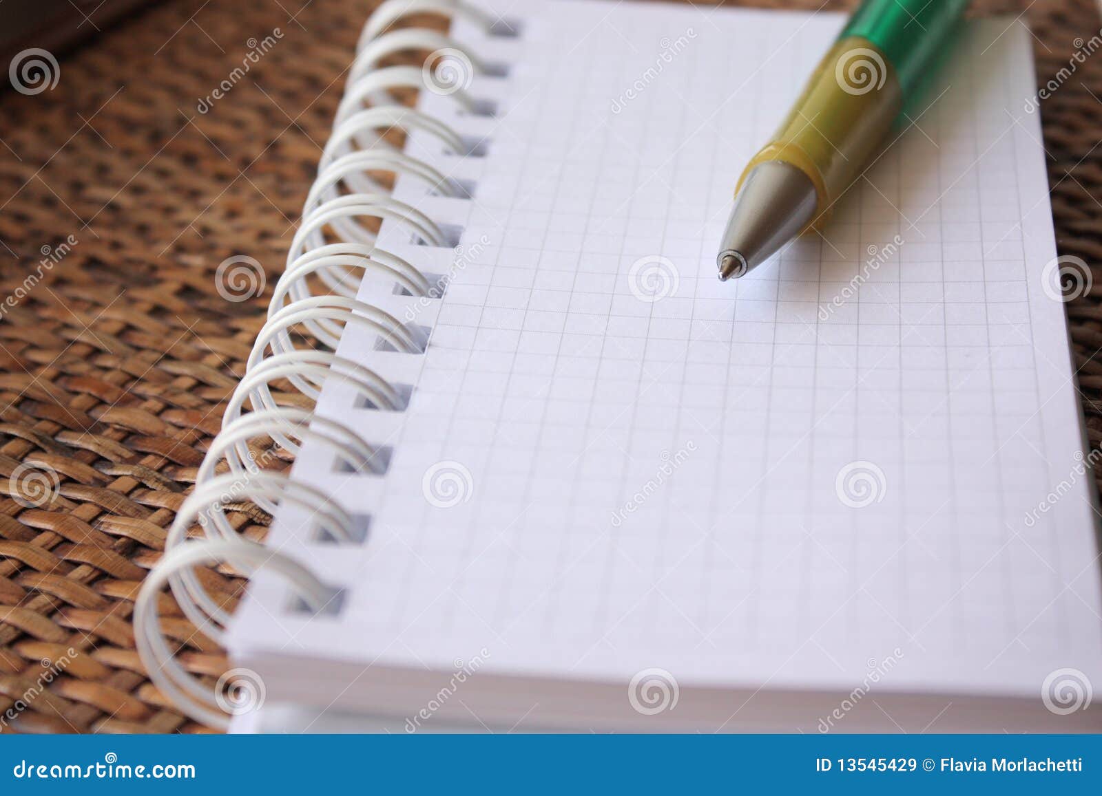 Spiral bound notebook with pen over rattan desk- shallow dof