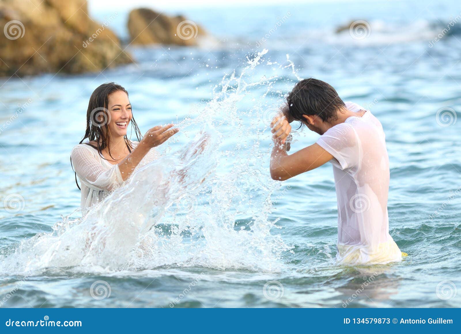 spontaneous couple joking throwing water on the beach