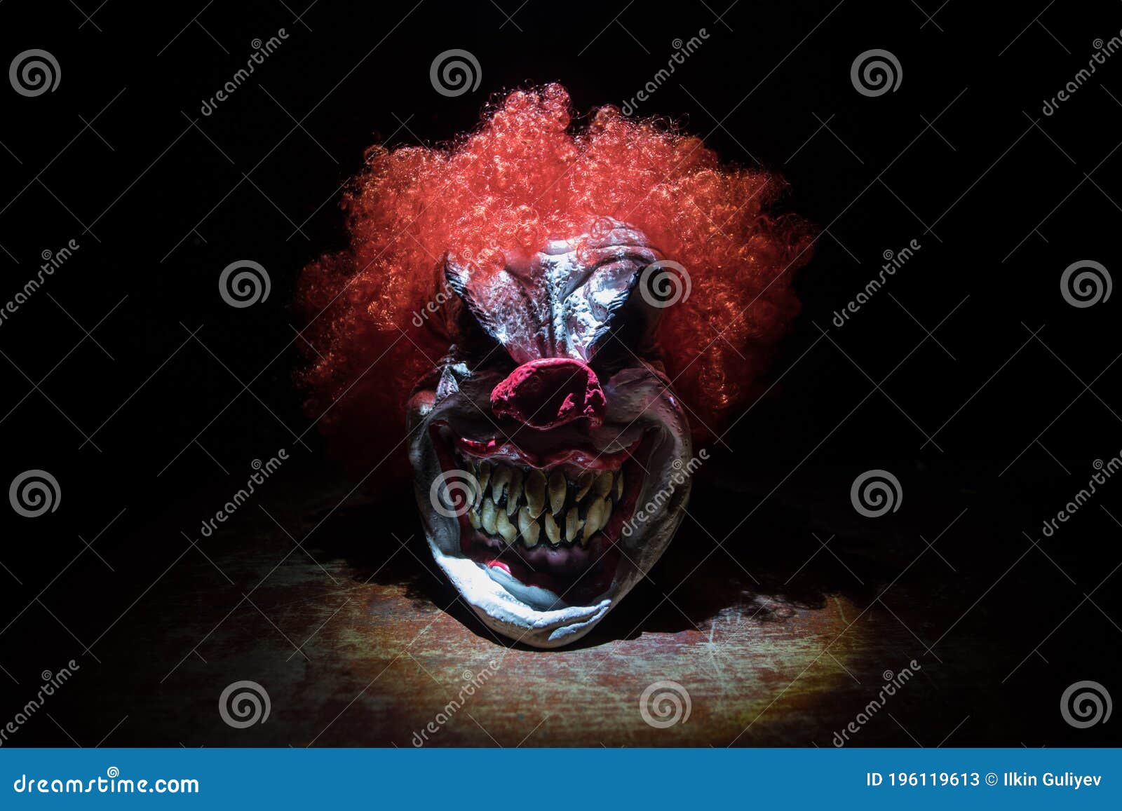spooky clown head on wooden table. evil clown head smiling on dark foggy background. halloween concept