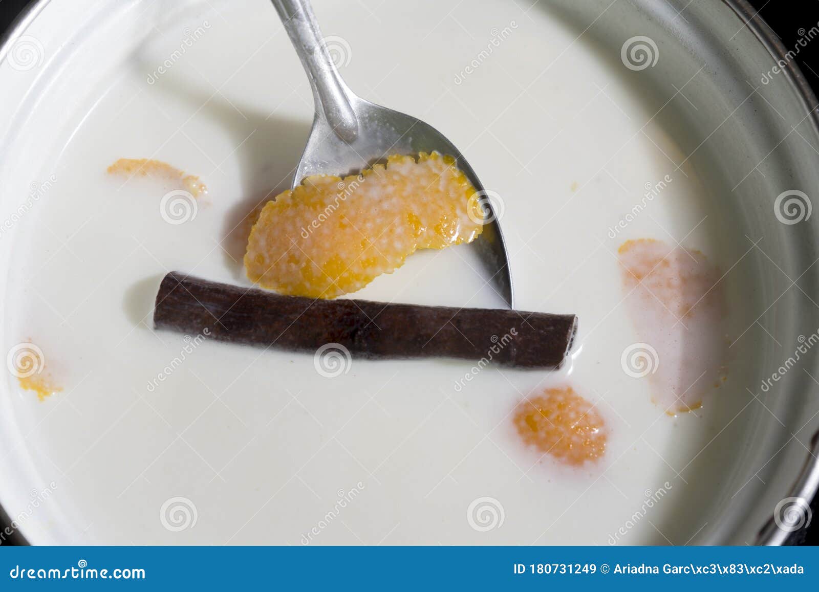 a spoon with a cinnamon stick inside a saucepan with milk and orange peel.