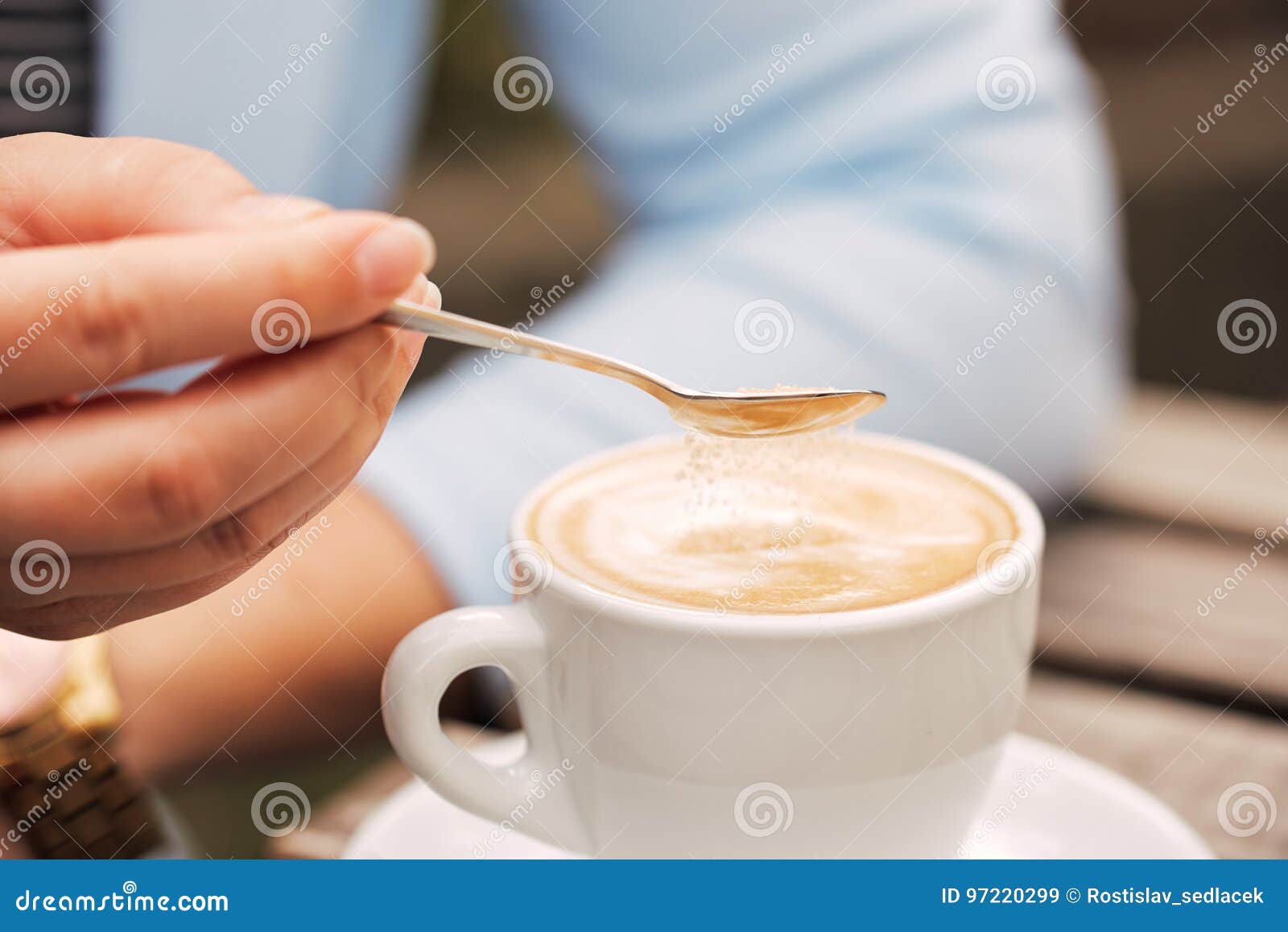 Close-up of a spoon in a female hand pouring sugar into her coffee cup