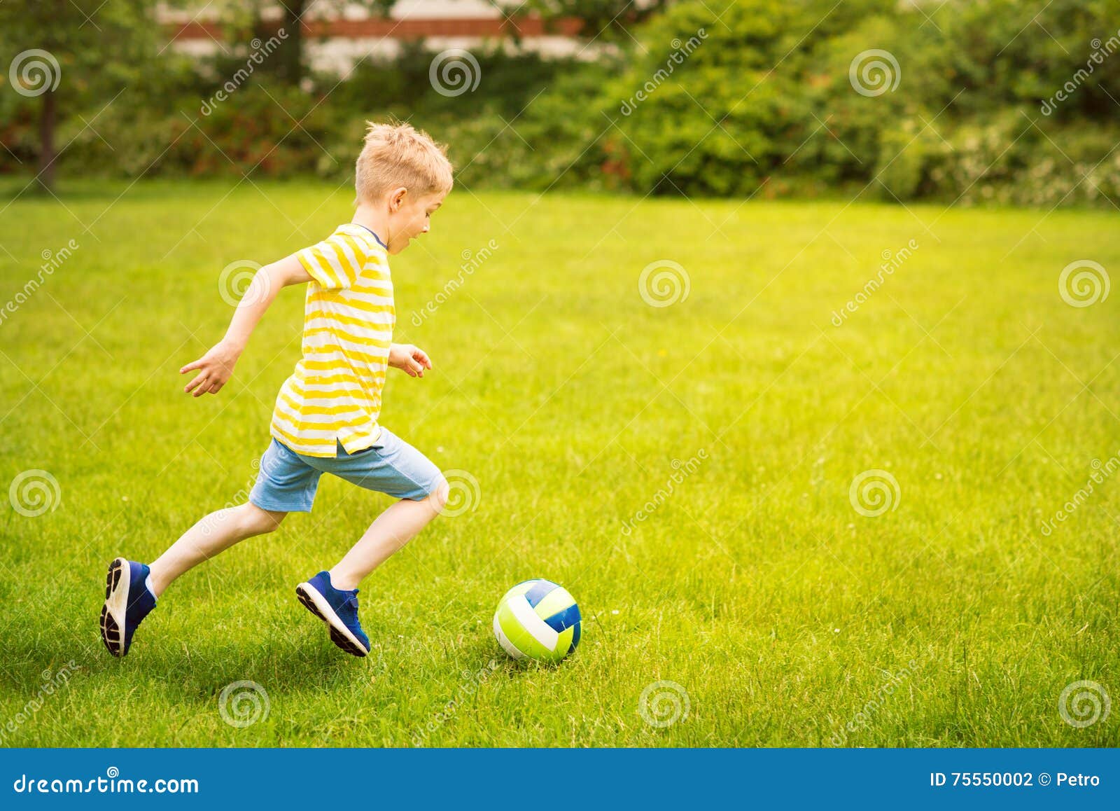 sporting boy plays football in sunny park
