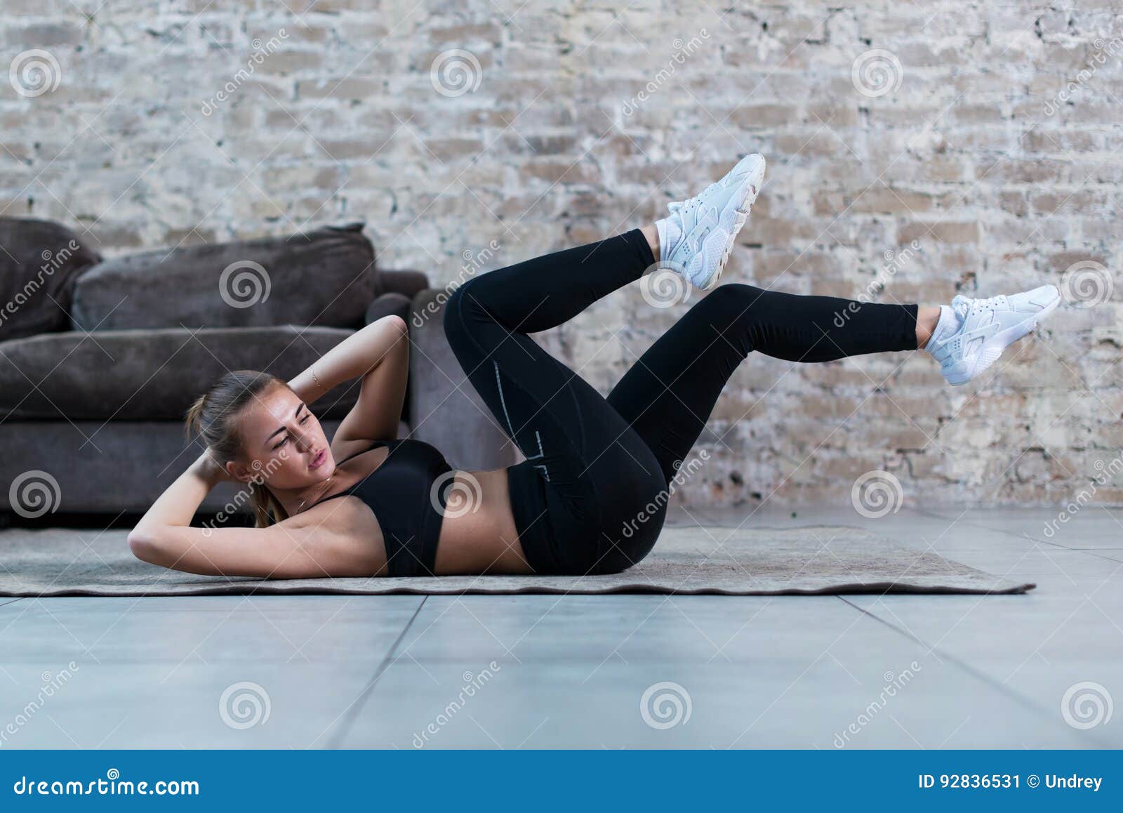 sportive young lady doing crisscross crunch exercise lying on a rug at modern studio