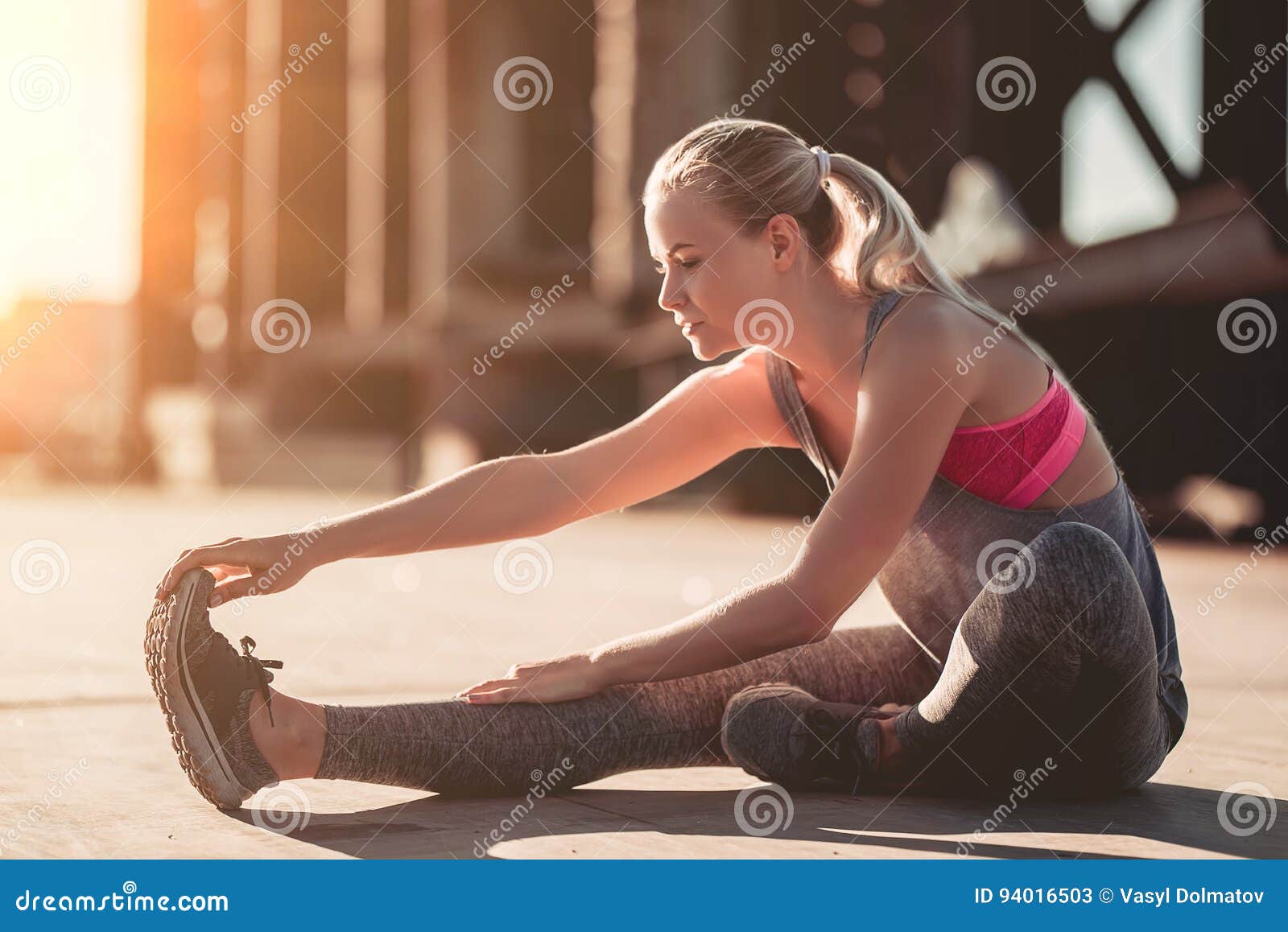 Sportliches Mädchen auf Straße. Attraktives sportliches Mädchen dehnt auf Straße während des Sonnenuntergangs aus