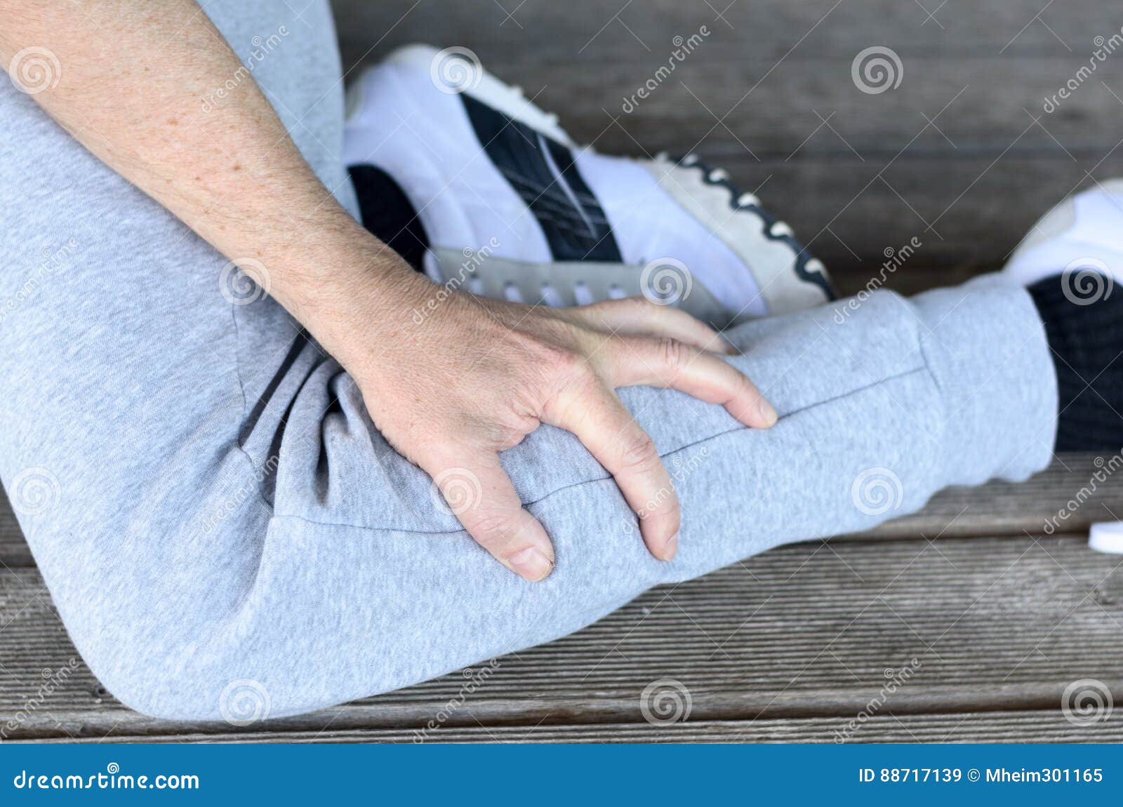 Sportsman with a muscle spasm in his calf. Sportsman with a muscle spasm or cramp in his calf clutching his lower leg with his hand in a close up view on a wooden deck