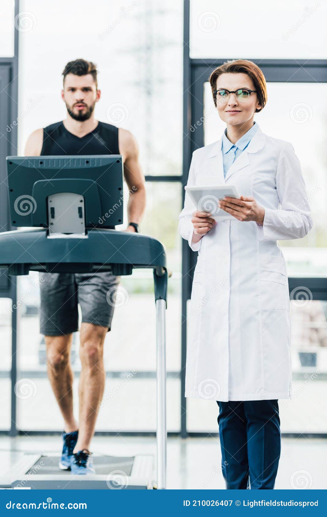 Sportsman Running On Treadmill Near Attractive Doctor During Endurance