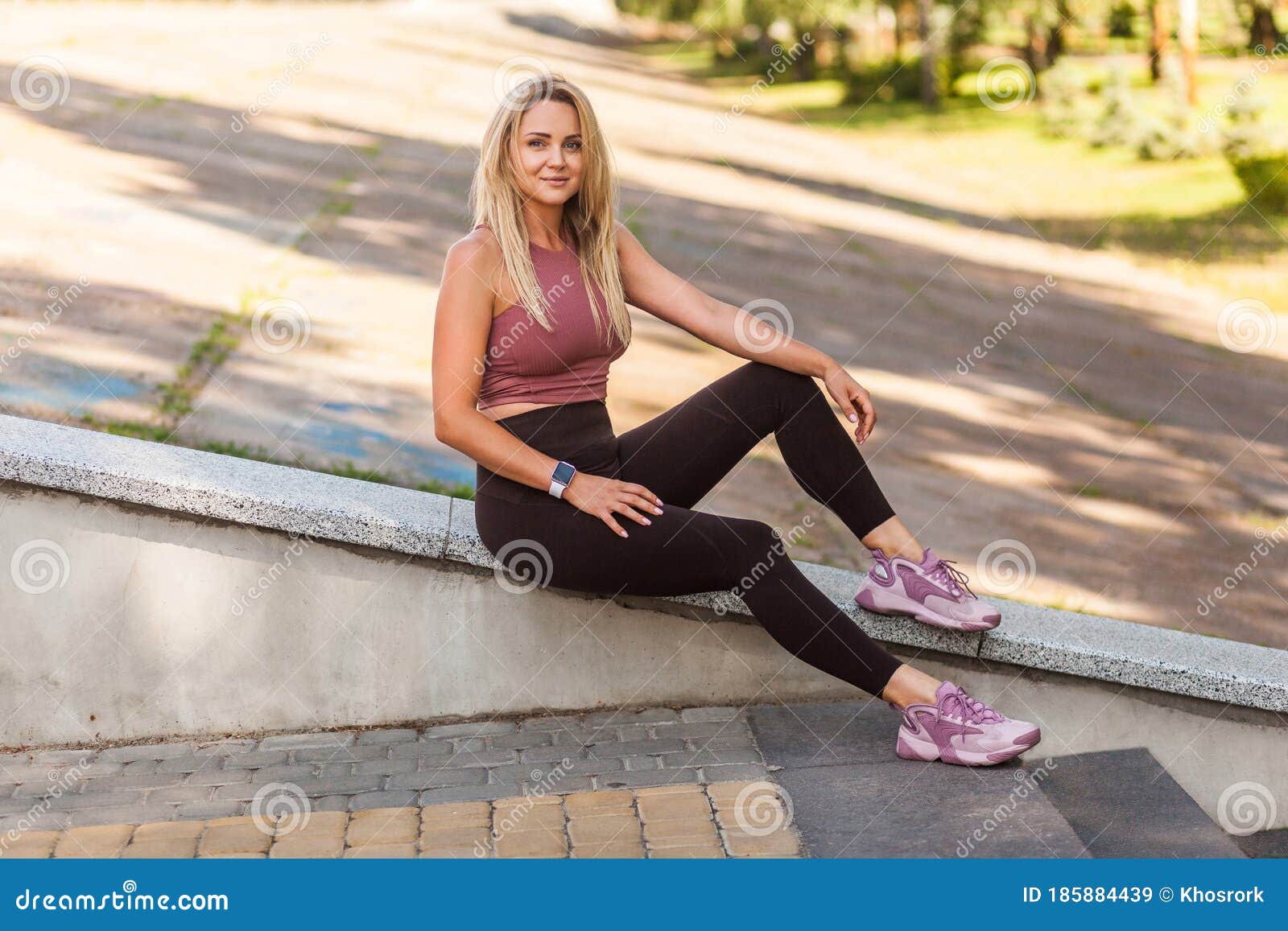 A young woman stretching in fitness clothing while leaning on a bench with  her legs straight and the sun on her skin Stock Photo  Alamy