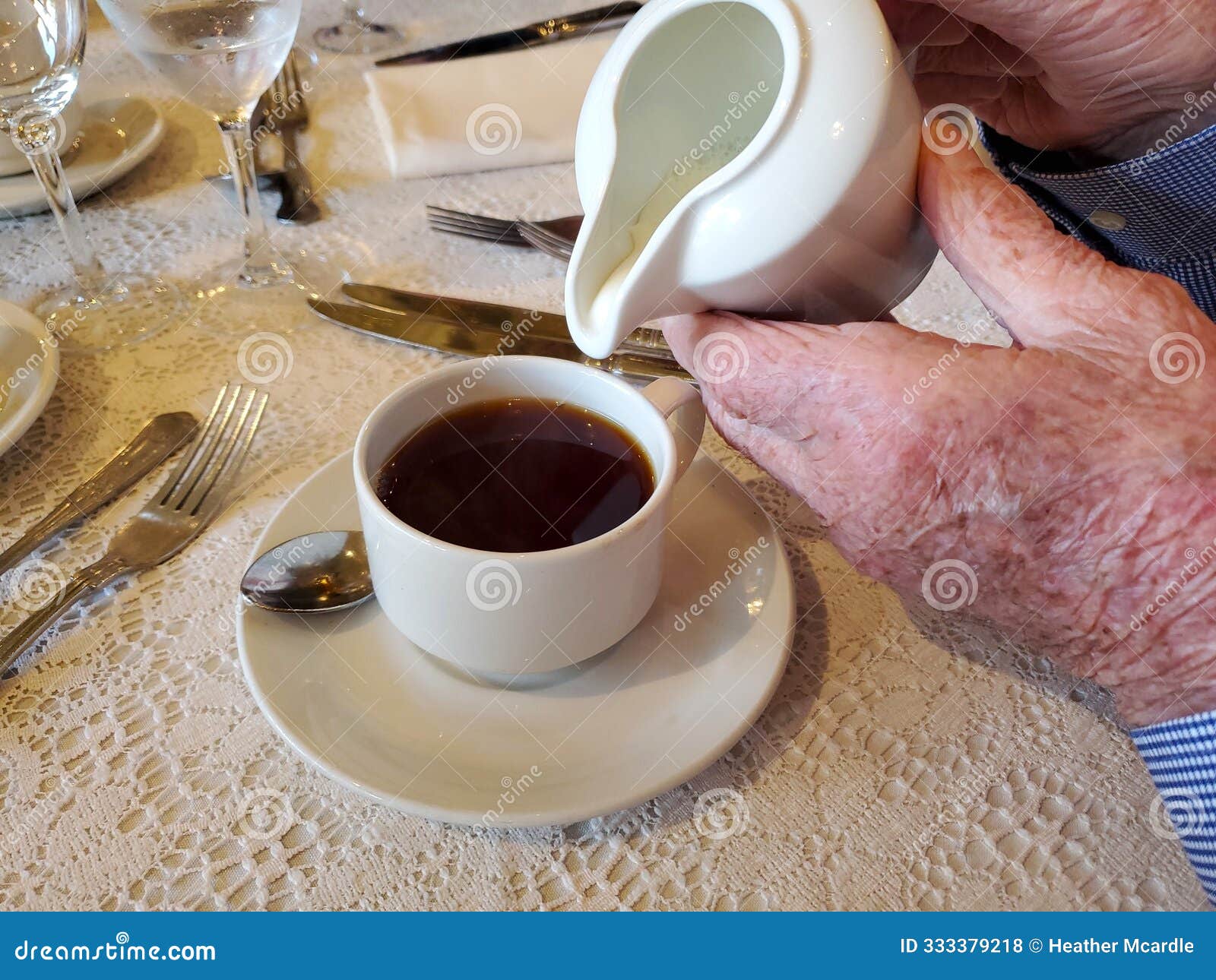 elderly hands pour cream into cup of coffee on decorative table