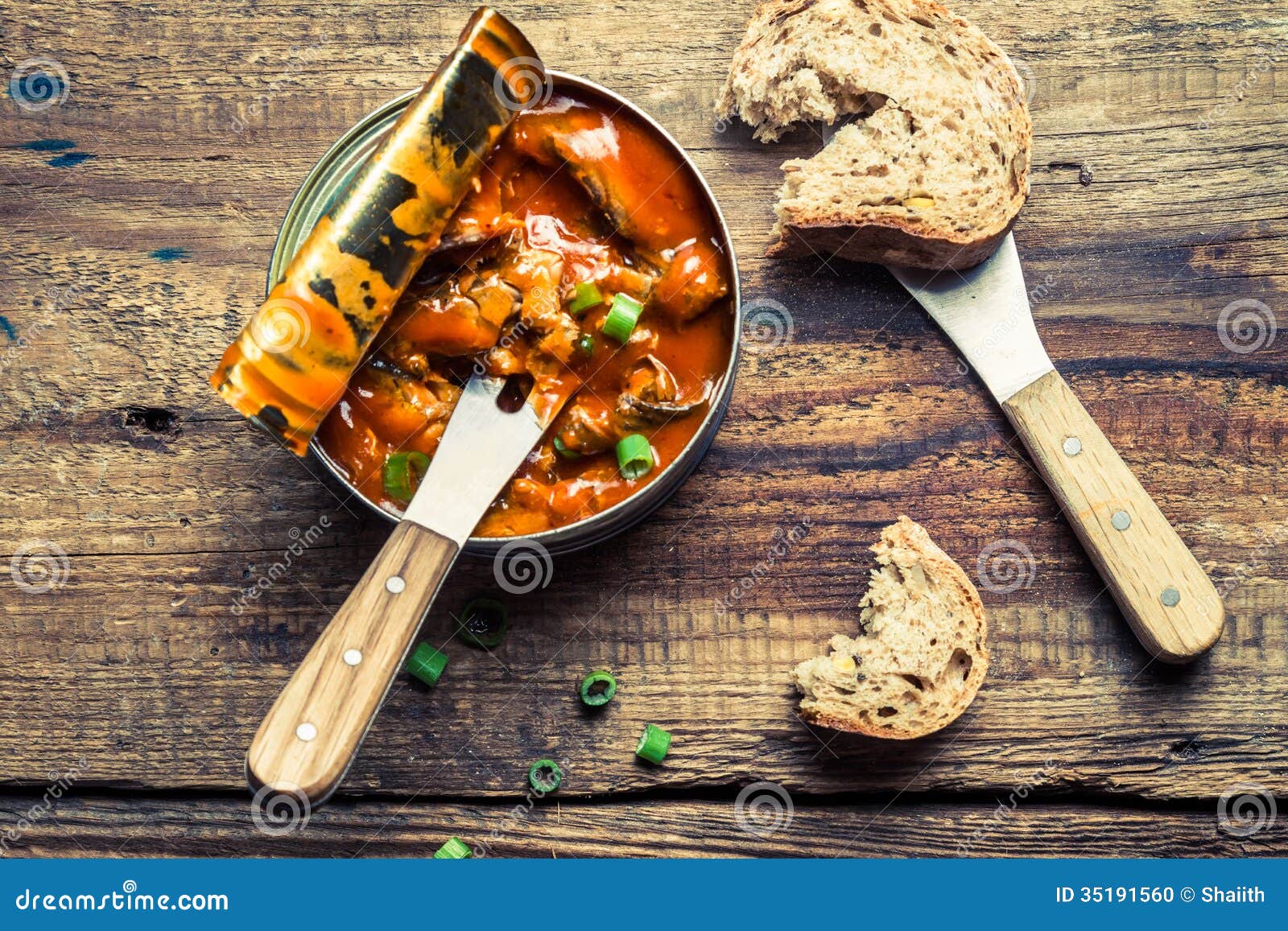 Sprat in tomato sauce with chives on old wooden table