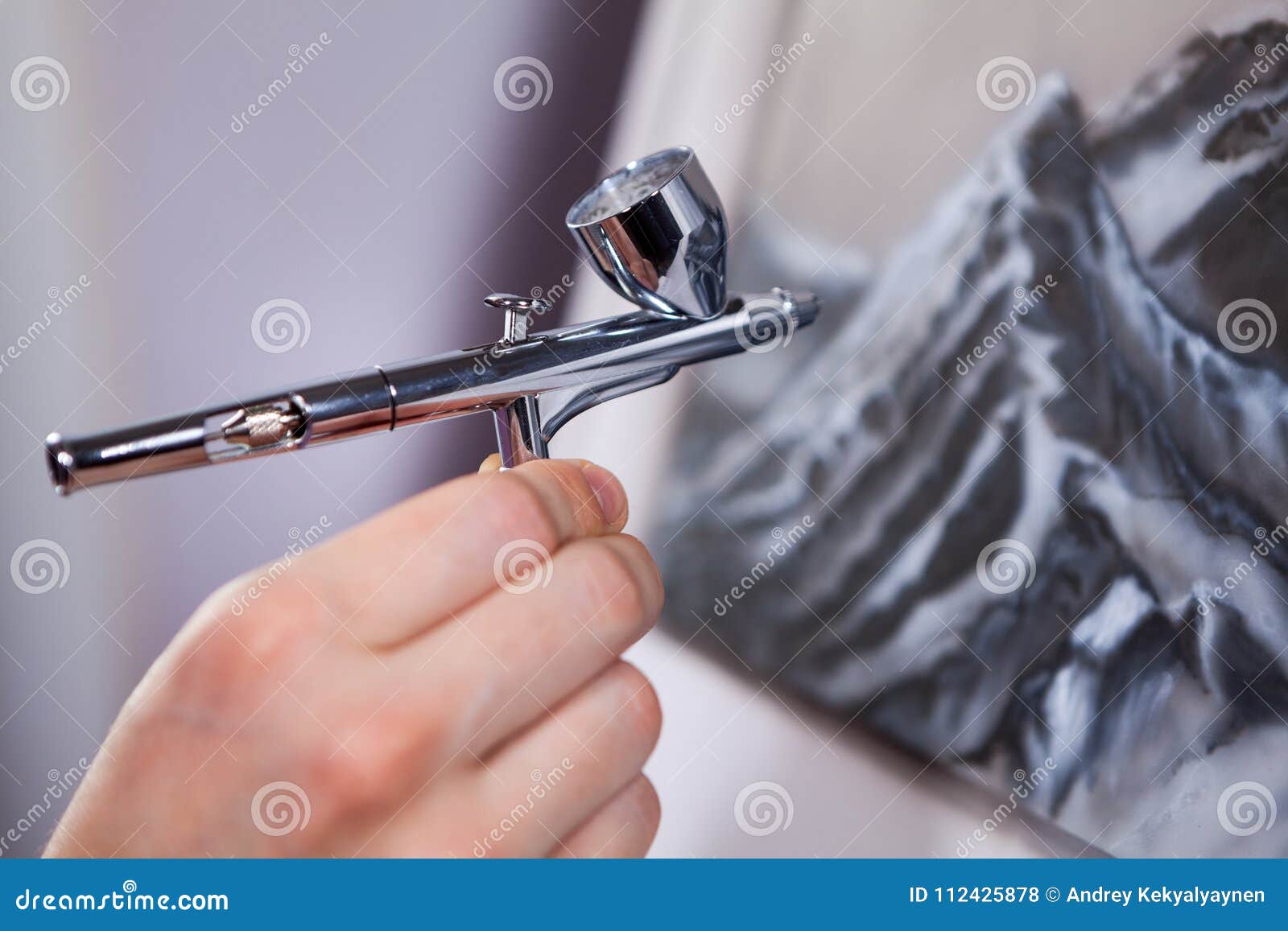 spraying gun an air brush in female hand, painting mountains with aerograph, close up view