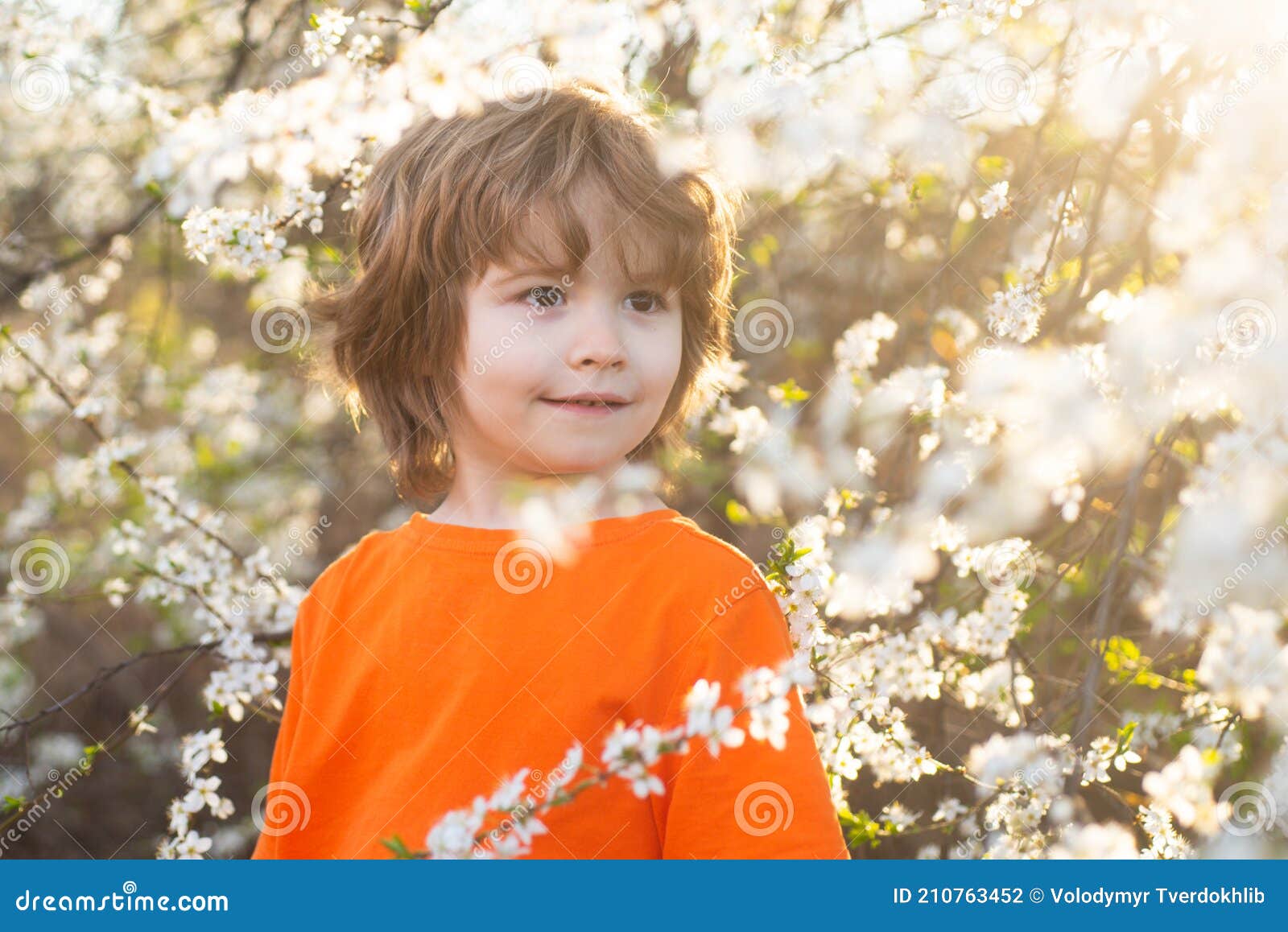 Spring Boy in Blooming Park. Smiling Kid Outdoor. Blooming Tree in Park